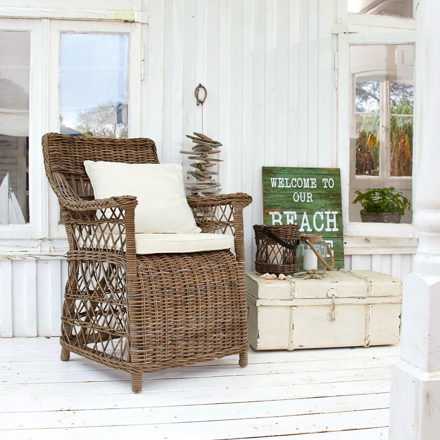 Rattansessel mit cremefarbenem Kissen auf weißer Veranda mit Stranddeko