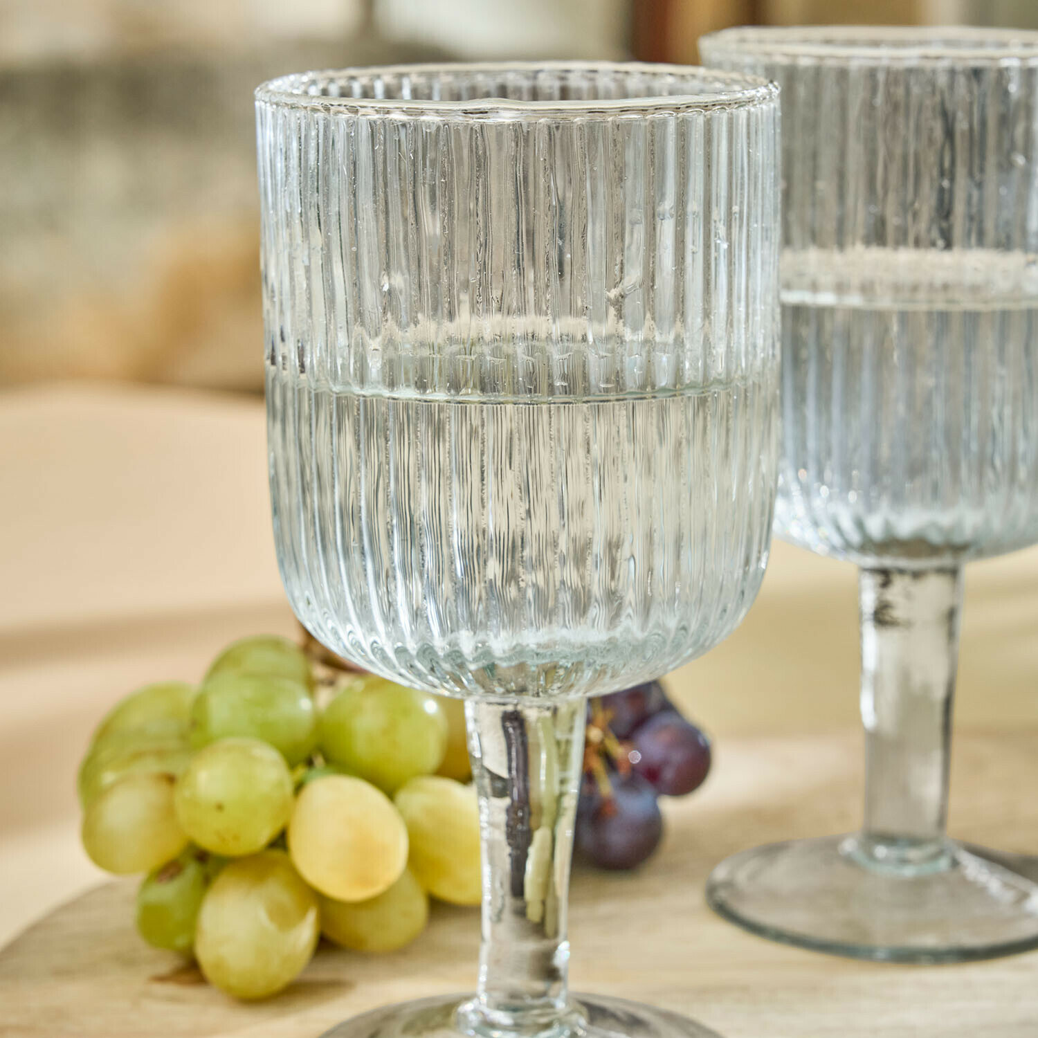 Transparenter, gerillter Glas-Weinkelch mit Wasser vor Trauben, elegantes Trinkglas