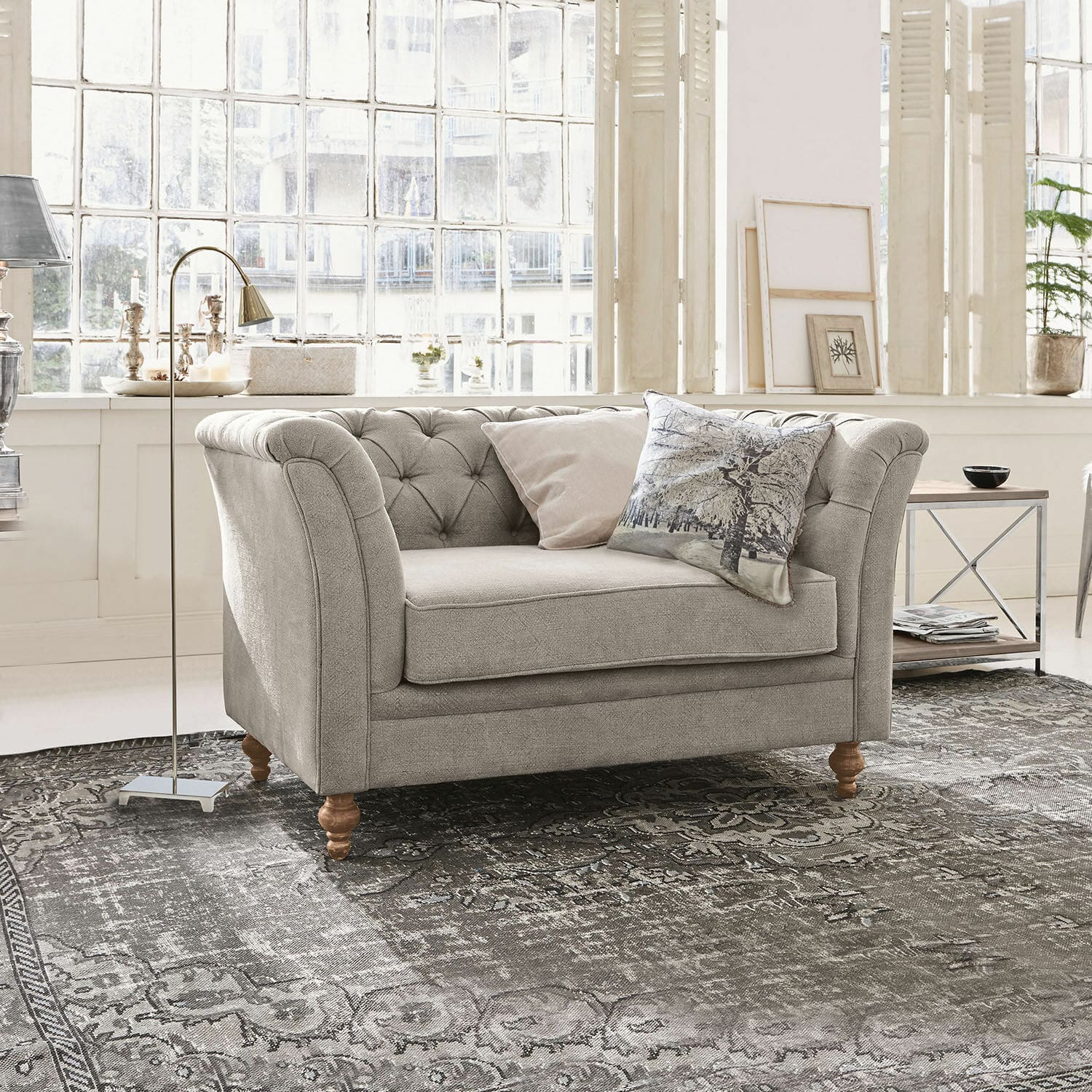 Grau gepolstertes Sofa mit Holzbeinen auf gemustertem Teppich in hellem Wohnzimmer