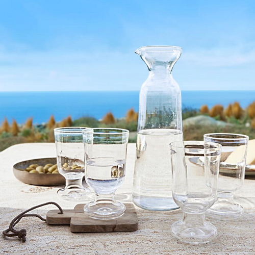 Glaskaraffe und vier durchsichtige Gläser auf Tisch mit Meerblick, klares Glas