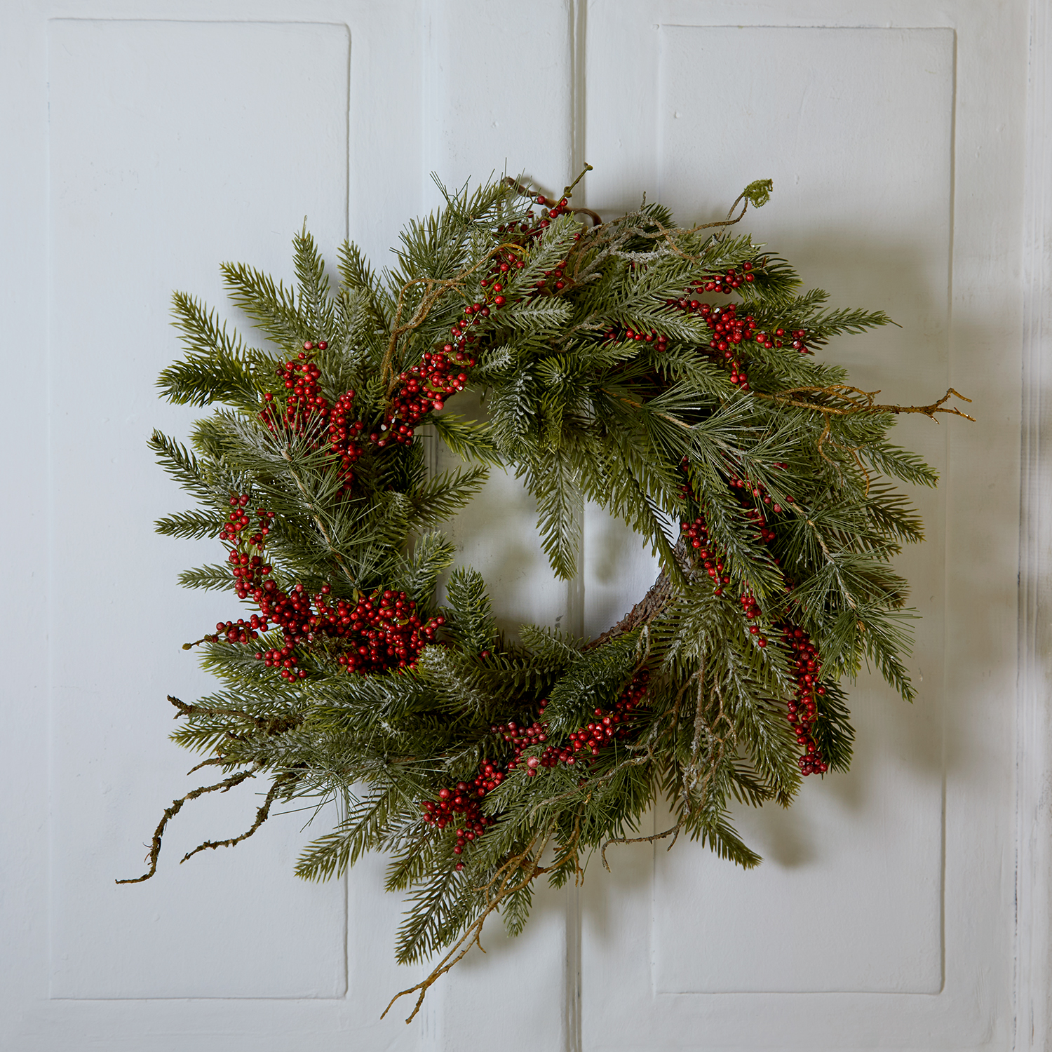 Weihnachtskranz aus grünen Zweigen und roten Beeren an weißer Tür, festliche Dekoration