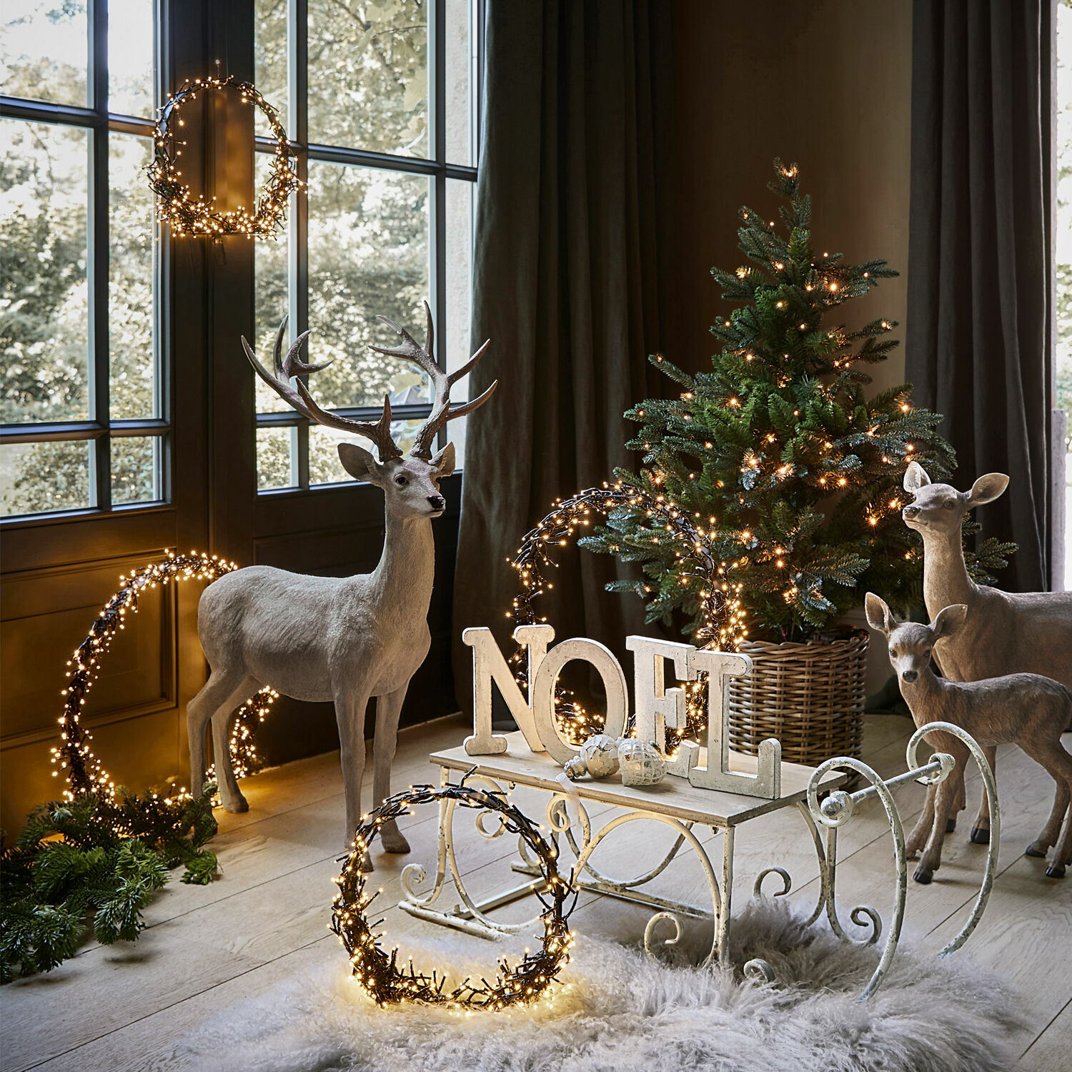 Weihnachtsdekoration mit Hirschfiguren, Tannenbaum im Korb und beleuchteten NOEL-Buchstaben