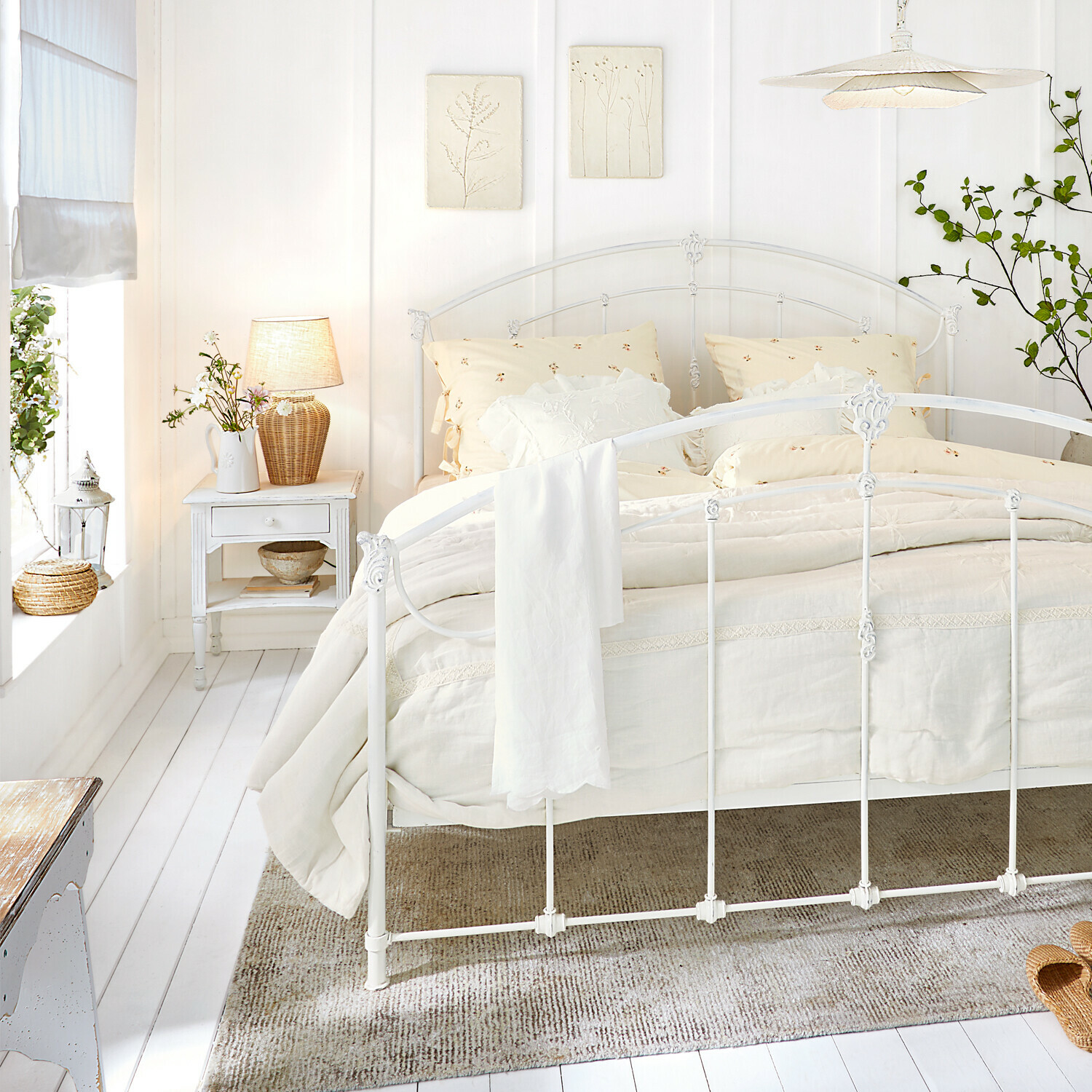 Weißes Metallbett mit cremefarbener Bettwäsche und natürlichen Dekorationen in hellem Schlafzimmer