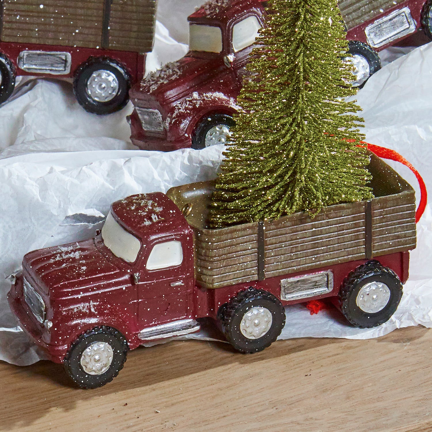 Rotes Metallmodell eines Lastwagens mit grünem Weihnachtsbaum, festliche Dekoration auf Holz