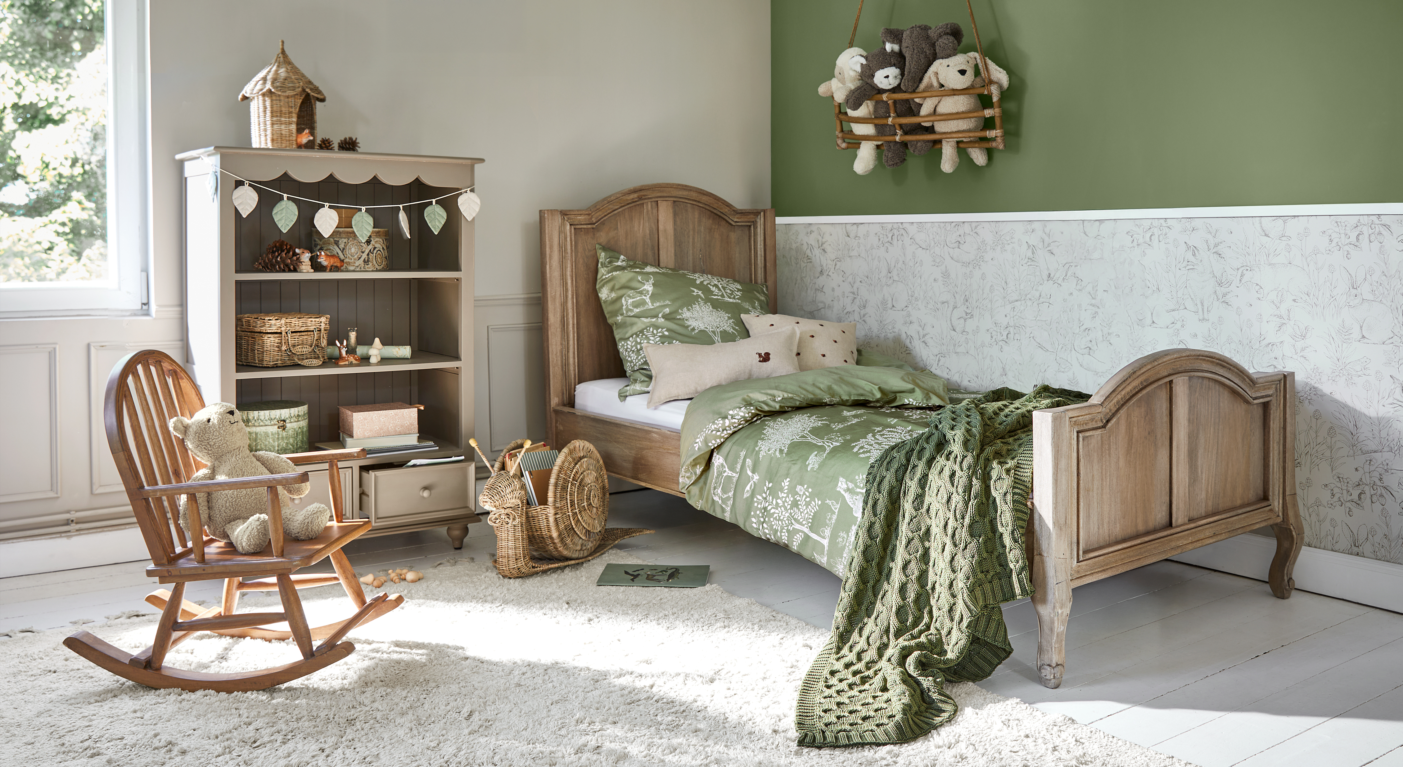 Kinderbett aus Holz mit grüner Bettwäsche und Decke, gemütliches Zimmer mit Schaukelstuhl und Teddybär