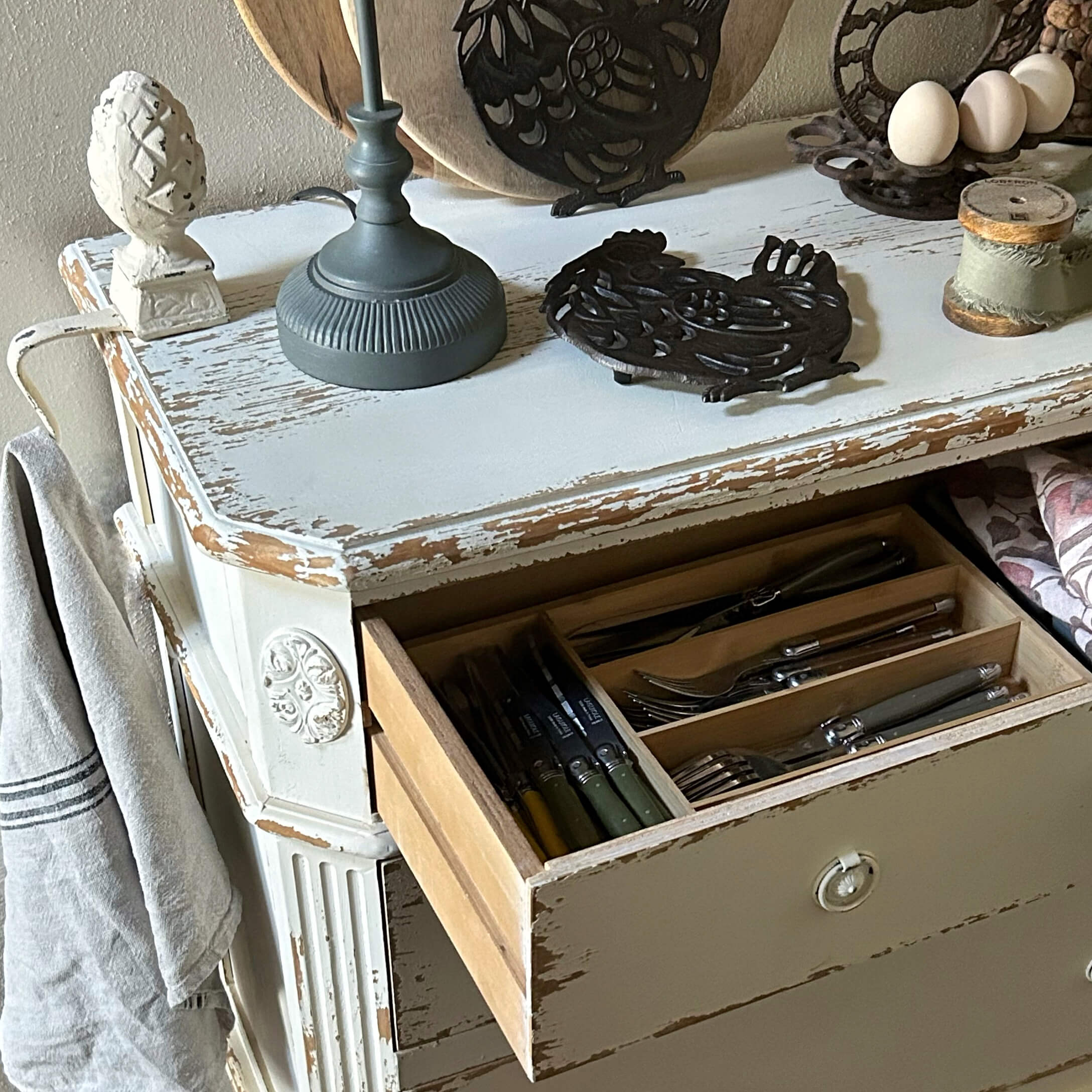 Weißer, shabby-chic Holzkommode mit geöffneter Schublade und Besteck-Organizer im Landhausstil