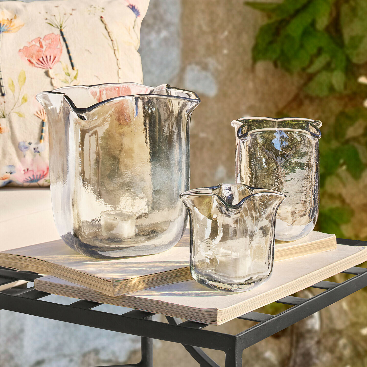 Set aus drei transparenten Glas-Teelichthaltern mit unregelmäßiger Form auf Büchern