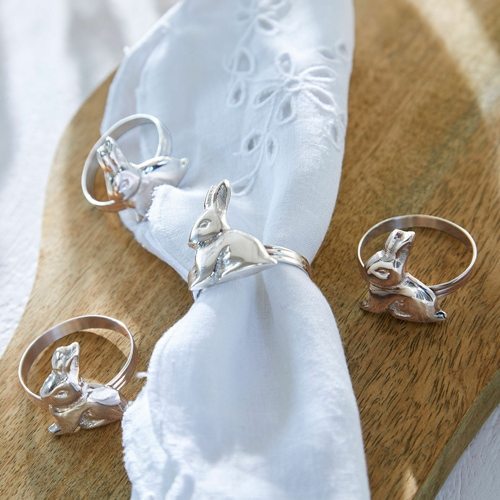 Silberne Ringe mit Hasenmotiv auf weißer Serviette auf Holzbrett, Tischdekoration