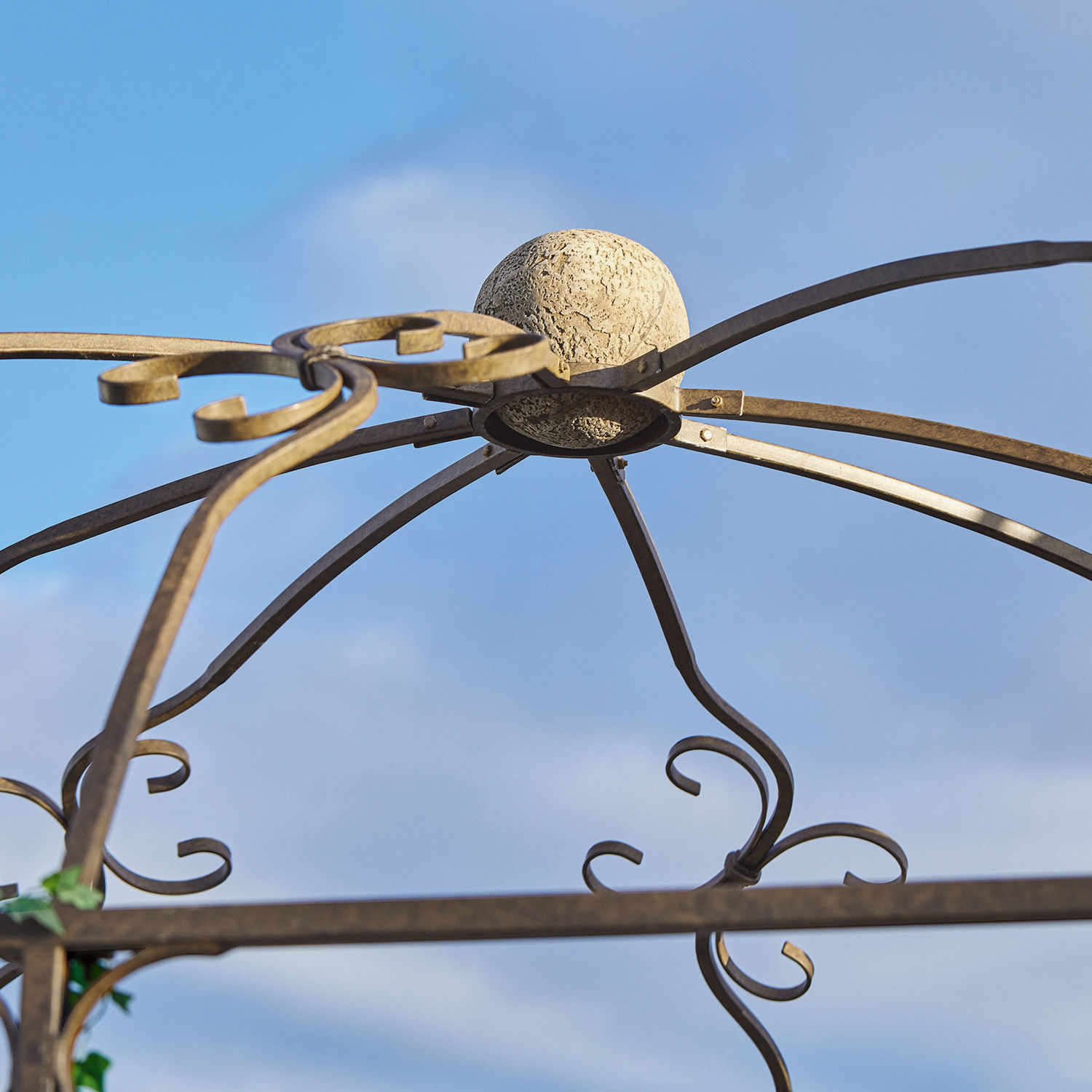 Metall-Gartenpergola mit dekorativem beigem Kugel-Element an der Spitze vor blauem Himmel