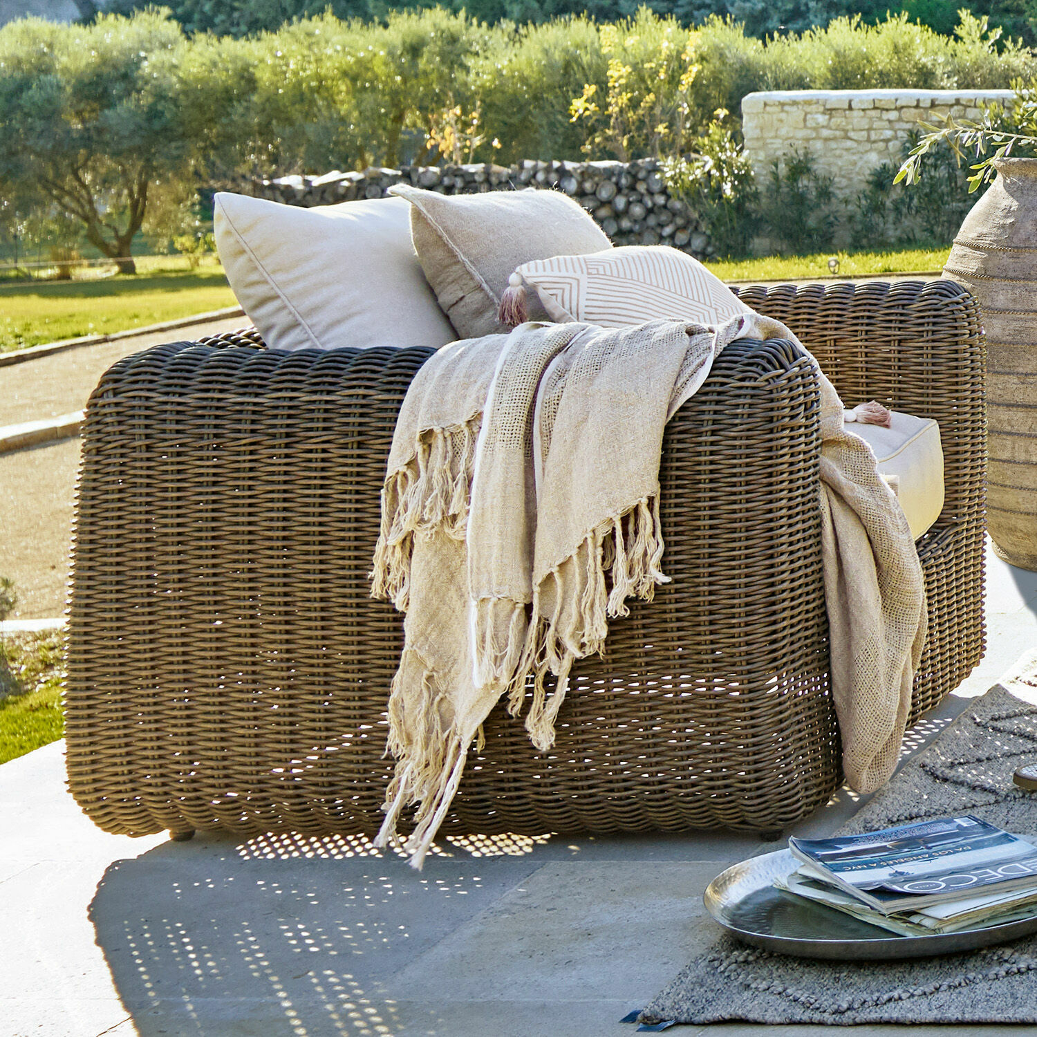 Brauner Rattan-Sessel mit cremefarbenen Kissen und beiger Decke auf der Gartenterrasse
