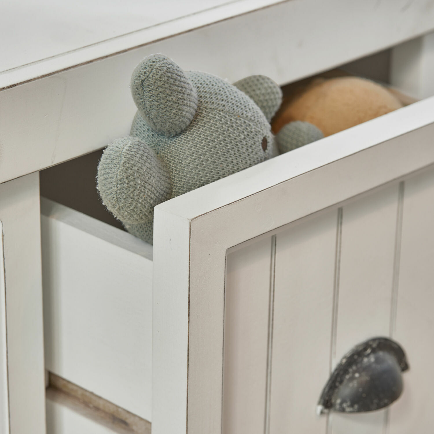 Weißes Holzmöbel mit geöffneter Schublade und grauem gestricktem Kuscheltier, Aufbewahrung