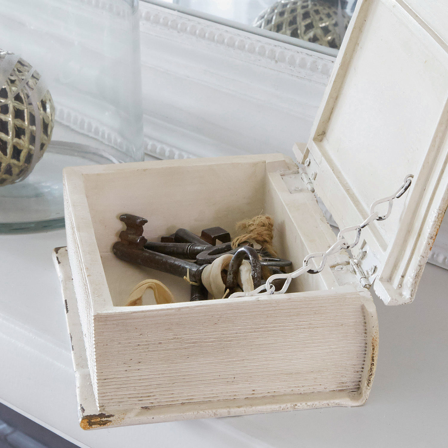 Weiße Holzbox in Buchform mit Metallschlüsseln auf weißem dekorativem Untergrund