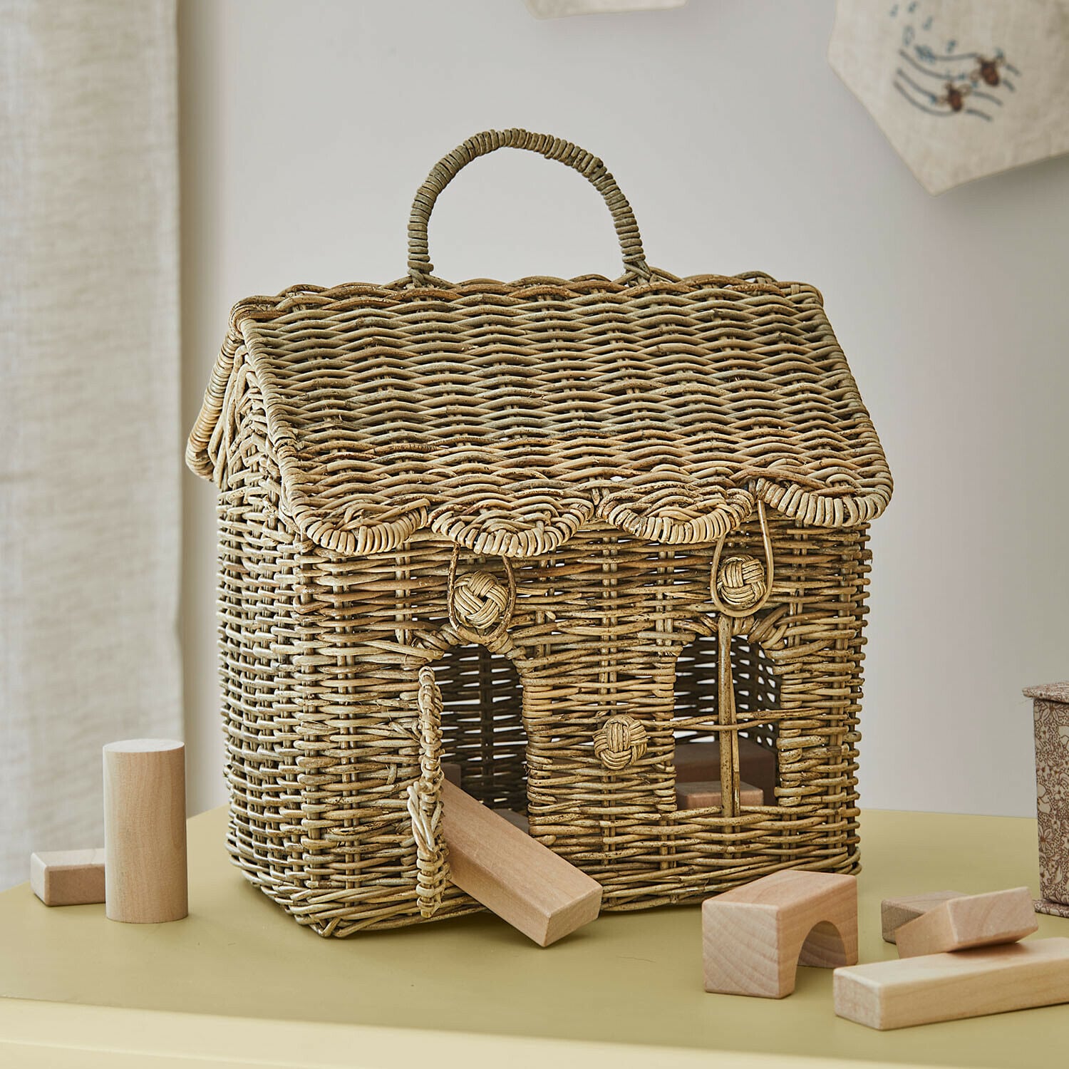 Haus aus natürlichem Weidengeflecht mit Holzbausteinen zum Spielen auf dem Tisch