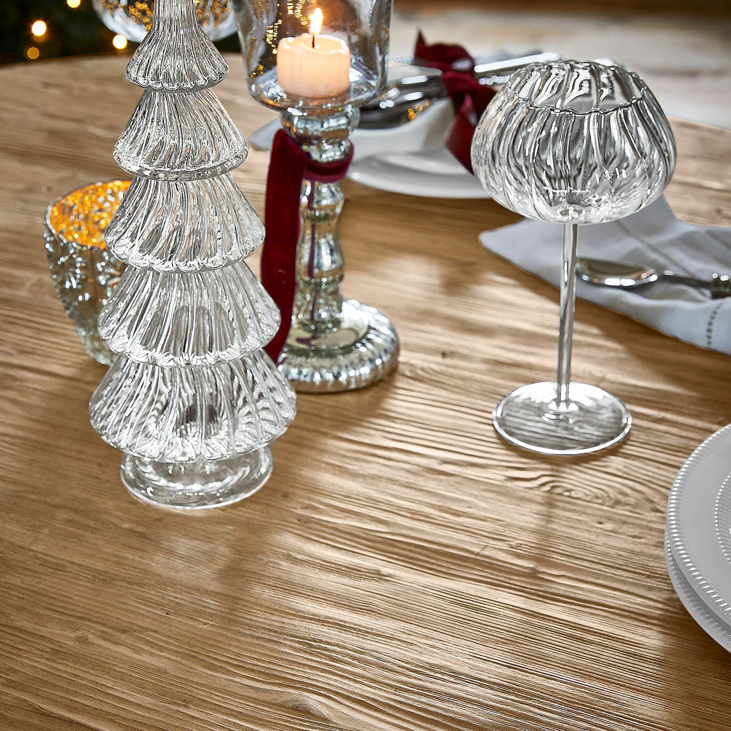 Glasdekorationen in Tannenbaum- und Kerzenhalterform auf Holztisch für festliche Tischdeko