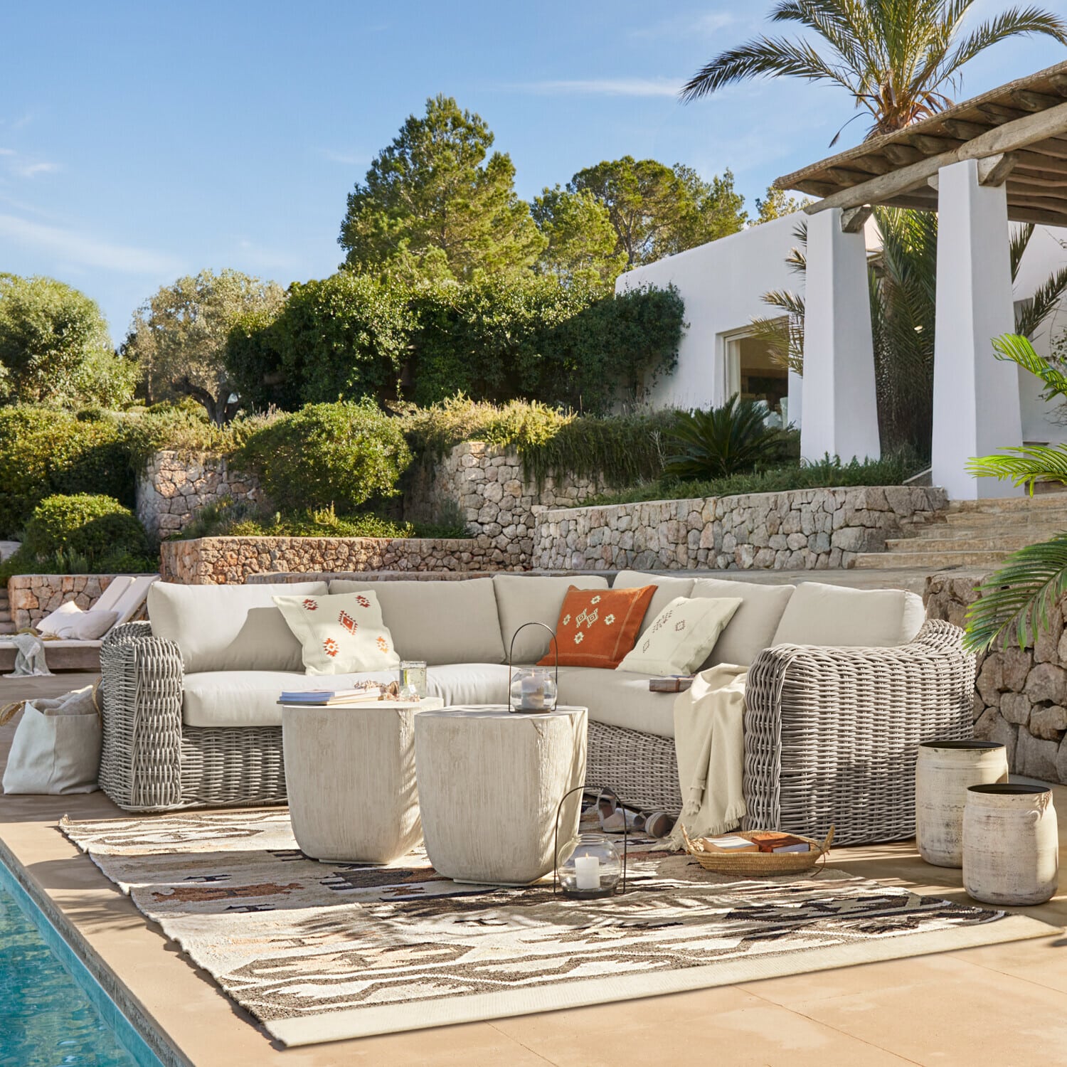 Gartenmöbel-Set aus grauem Rattan mit cremefarbenen Kissen und dekorativen Kissen am Pool
