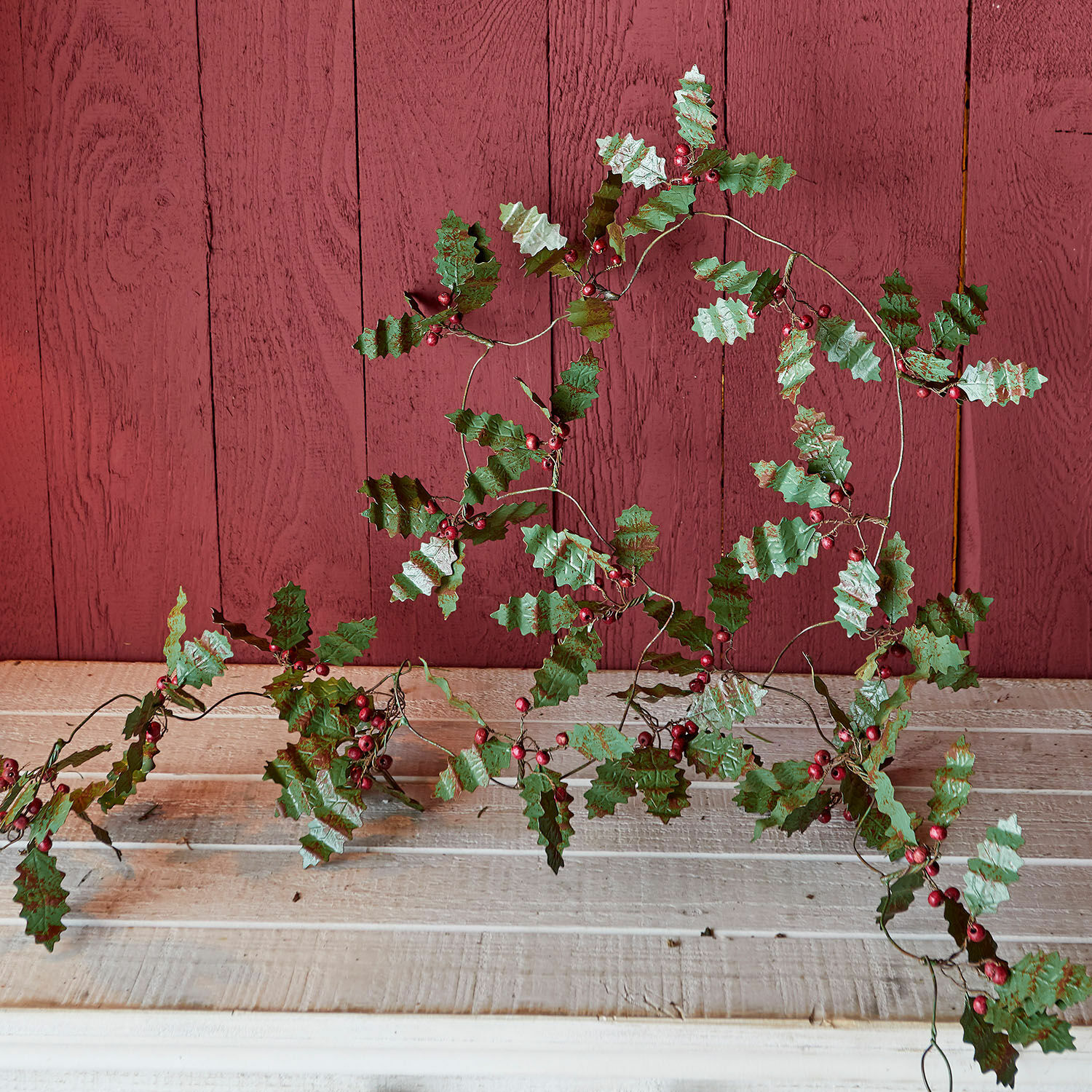 Dekorative Girlande mit grünen Blättern und roten Beeren auf Holzhintergrund, Weihnachtsdeko