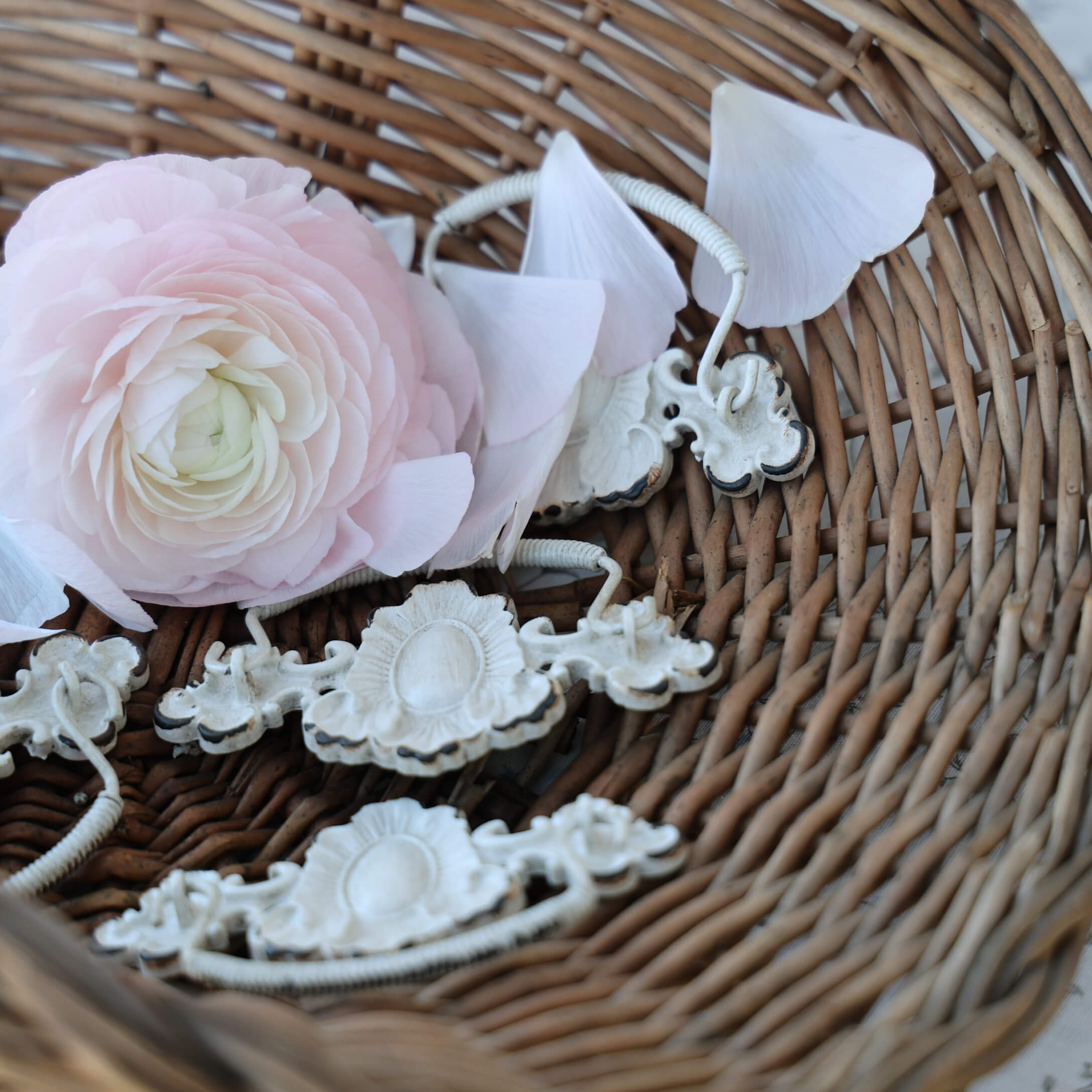 Zarte rosa Blume und weiße Metallgriffe in einem Weidenkorb, Vintage-Innendekoration