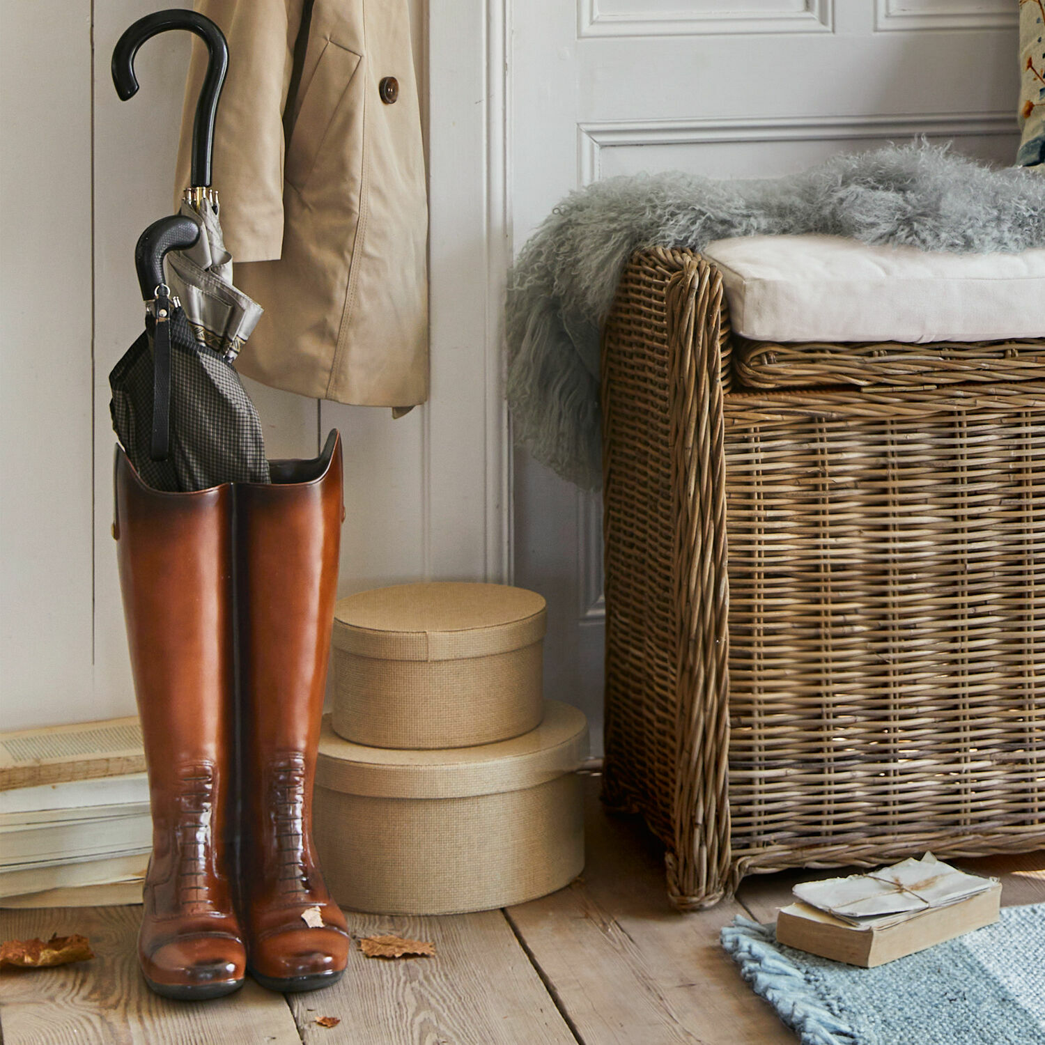 Braune hohe Lederstiefel mit Regenschirm innen, neben einem Korbmöbel und beigen Boxen