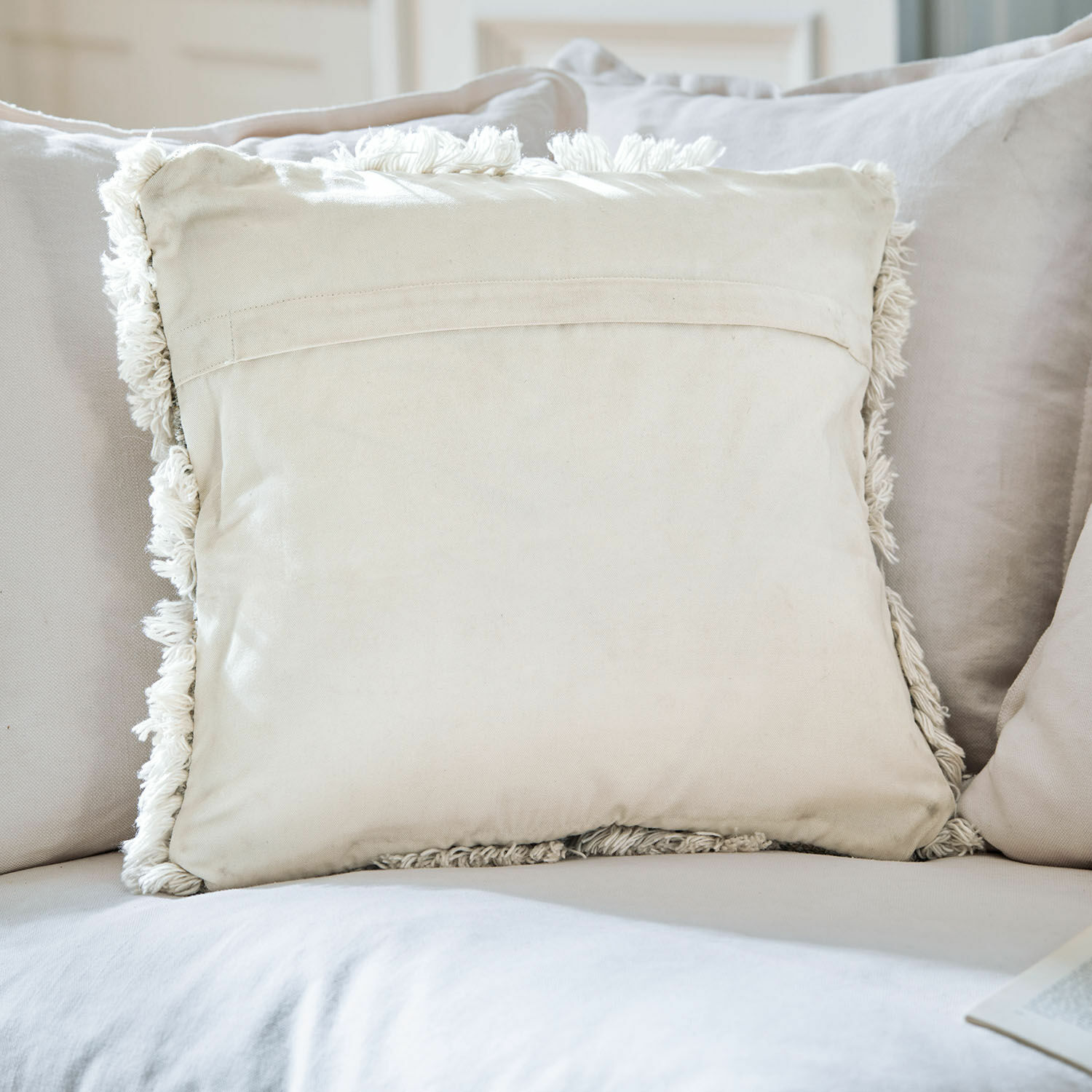 Beige Baumwoll-Dekokissen mit Fransen auf hellem Sofa für gemütliches Wohnzimmer