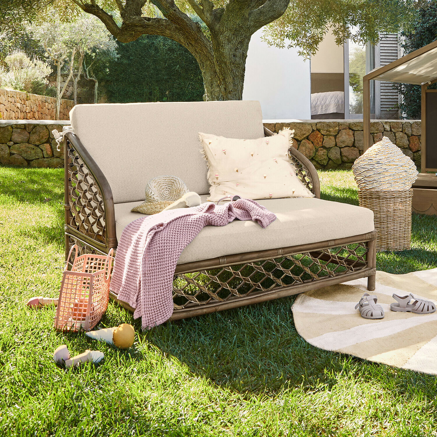 Rattansofa mit cremefarbenen Polstern auf grünem Rasen, Dekorationen und Decke