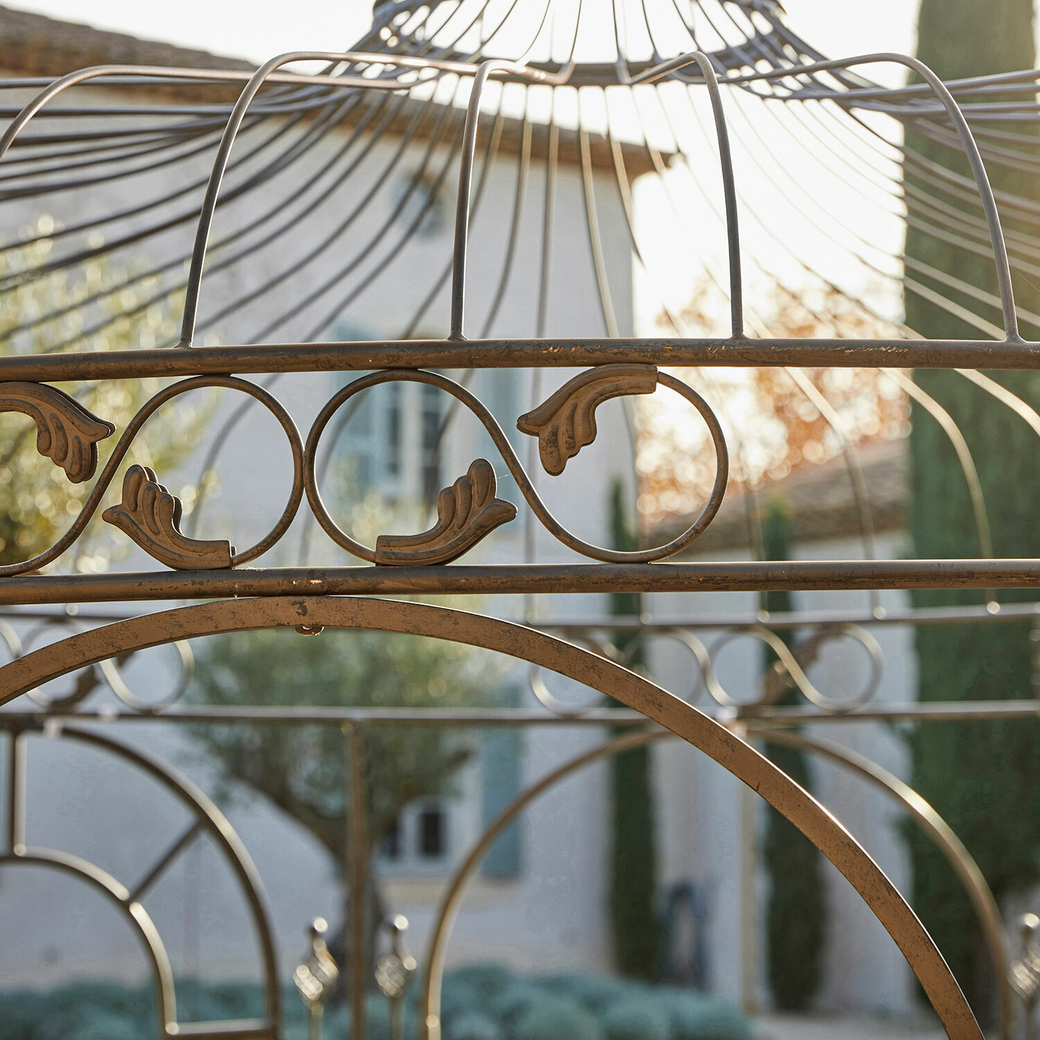 Metallische Zierstruktur in Altgold mit Blattmotiv vor Haus und Garten im Hintergrund