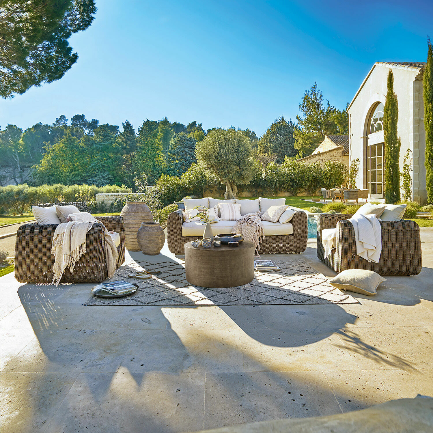 Sitzgruppe Bogdanne Braunes Rattan-Gartenmöbel-Set mit cremefarbenen Kissen auf Terrasse mit Blick auf grünen Garten