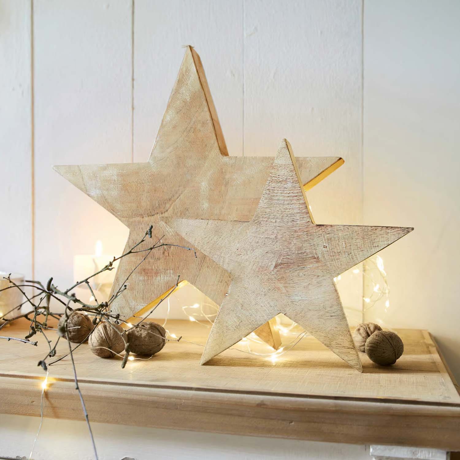 Holzsterne in Naturfarbe als Dekoration auf Tisch mit Walnüssen und LED-Lichterkette