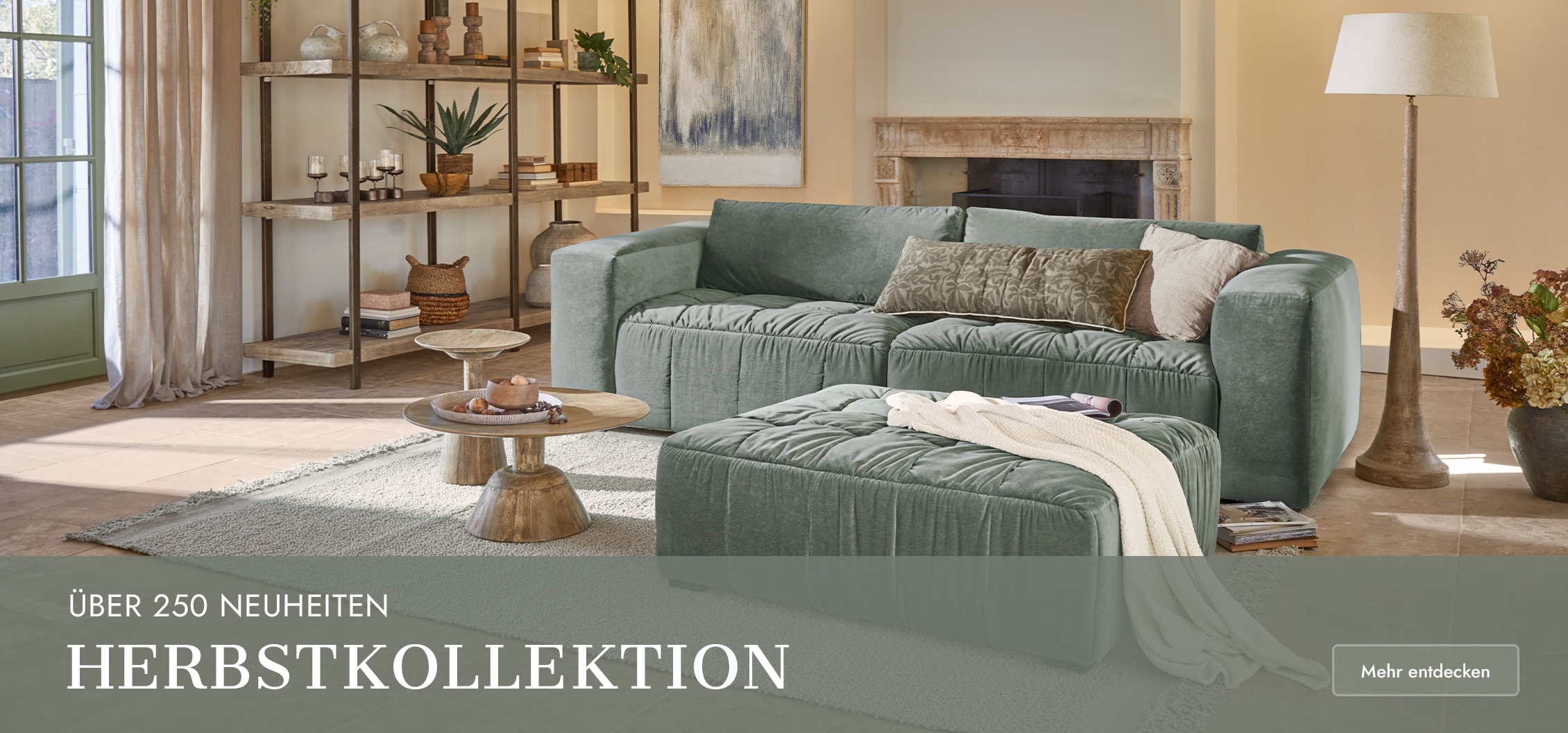 Grünes Samtsofa mit Hocker und Holztischen in hellem Wohnzimmer mit Kamin