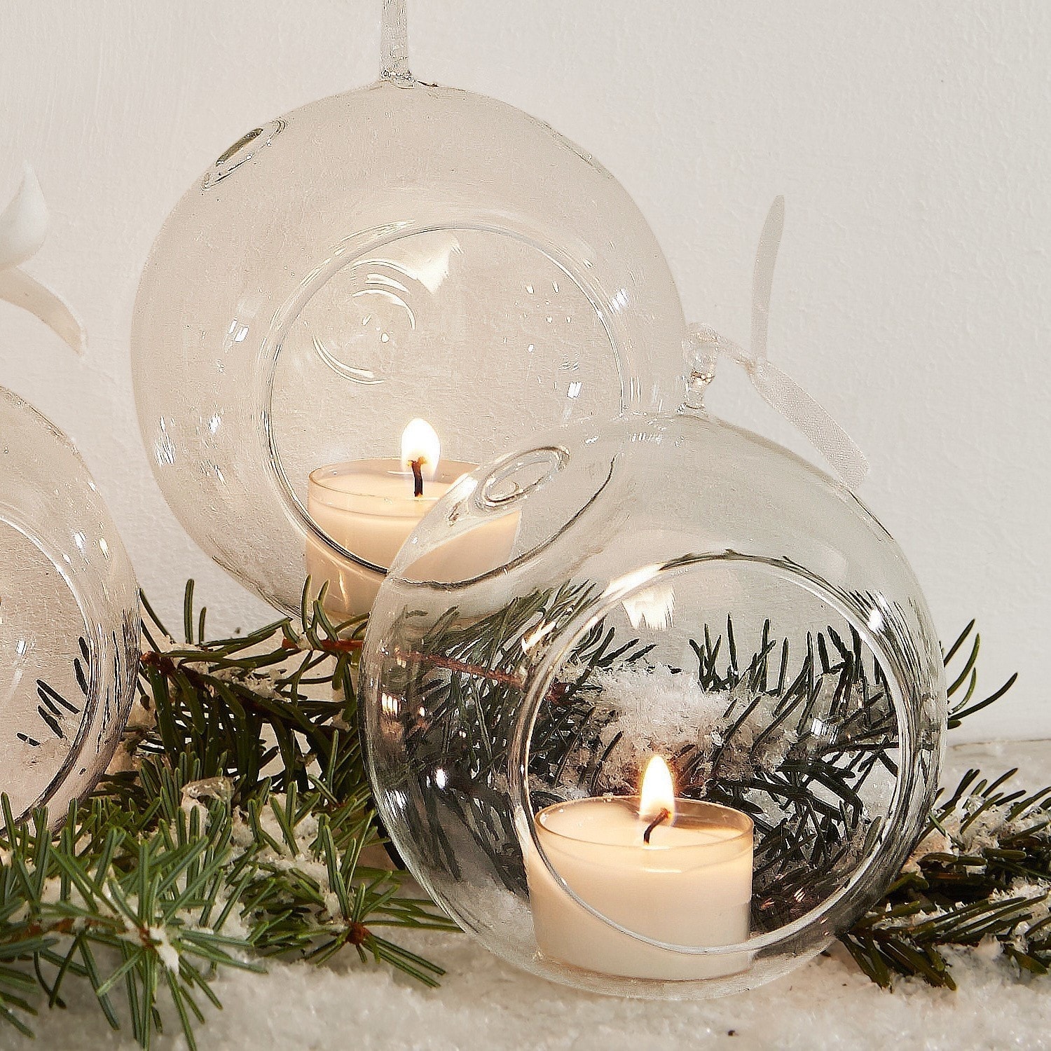 Transparente Glaskugeln mit Öffnungen für Teelichter, Weihnachtsdeko mit Tannenzweigen und Kunstschnee