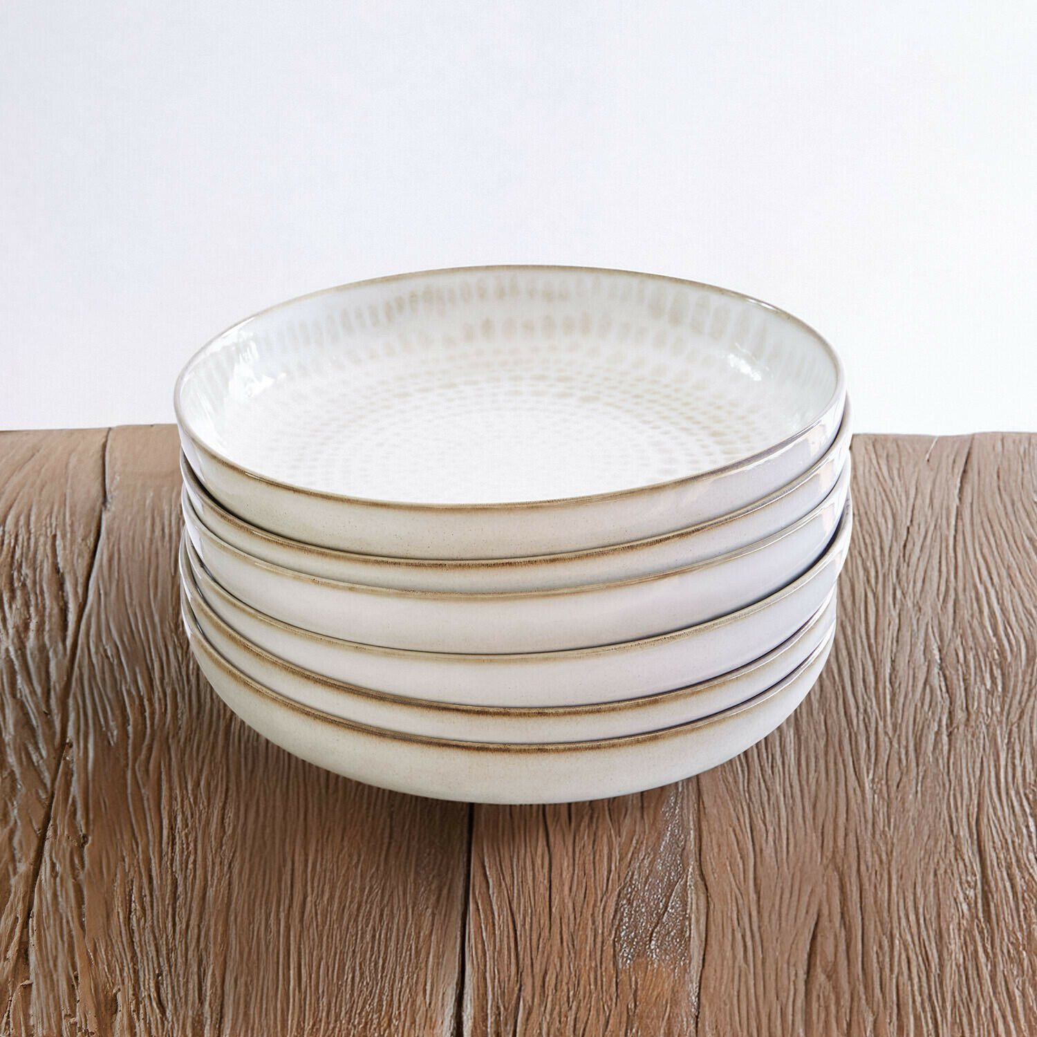 Fünf cremefarbene Keramikschalen mit feinem Muster auf einem Holztisch gestapelt