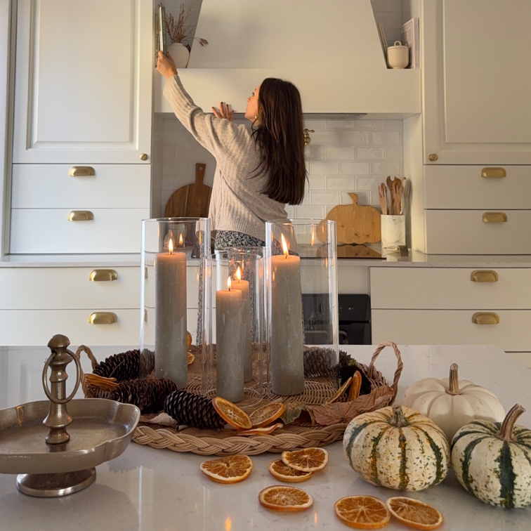 Herbstliches Ensemble mit grauen Kerzen in Glas, getrockneten Orangenscheiben und Kürbissen auf Küchentisch