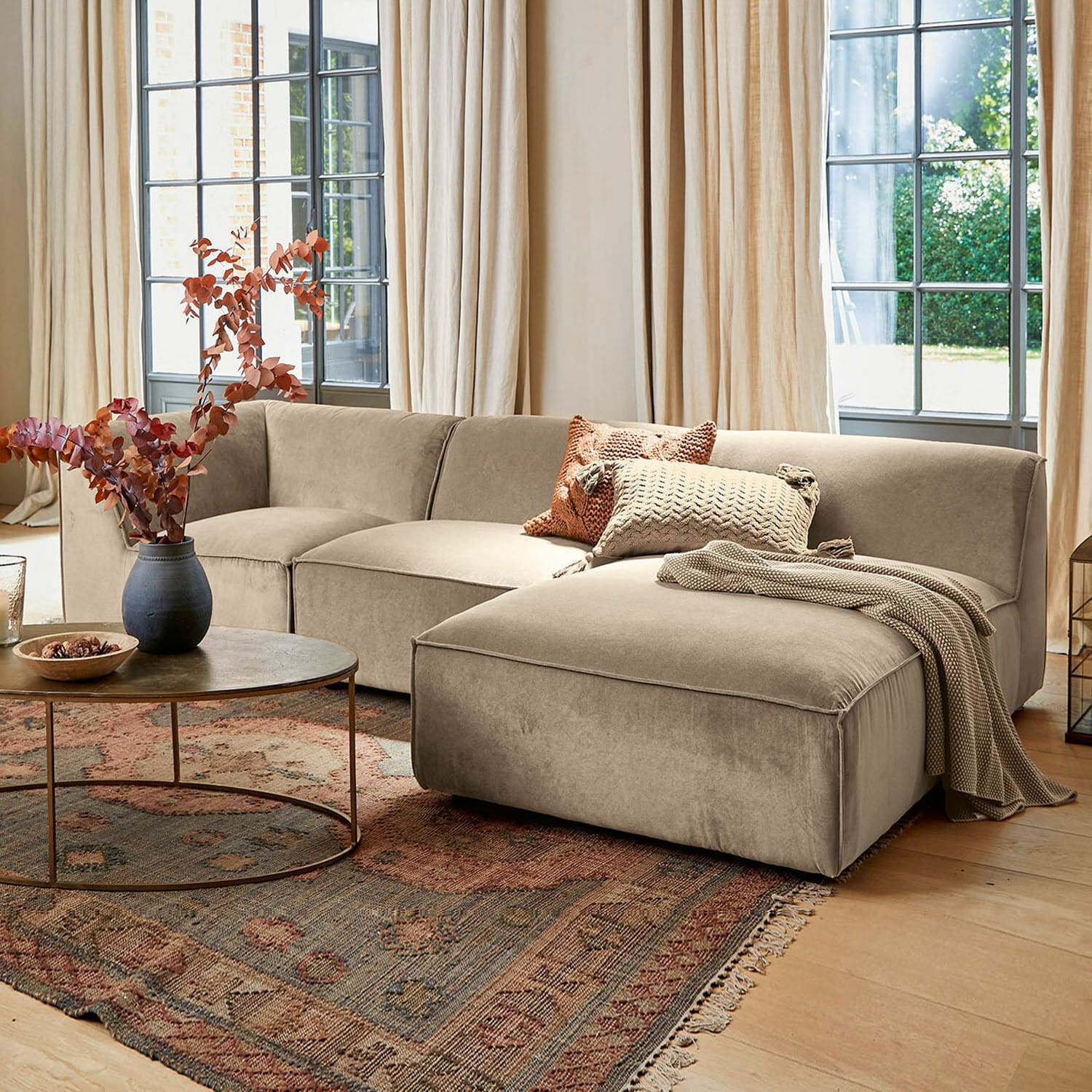 Sofa McLean Beige Ecksofa aus weichem Stoff in stilvollem Wohnzimmer mit Teppich und runden Couchtisch