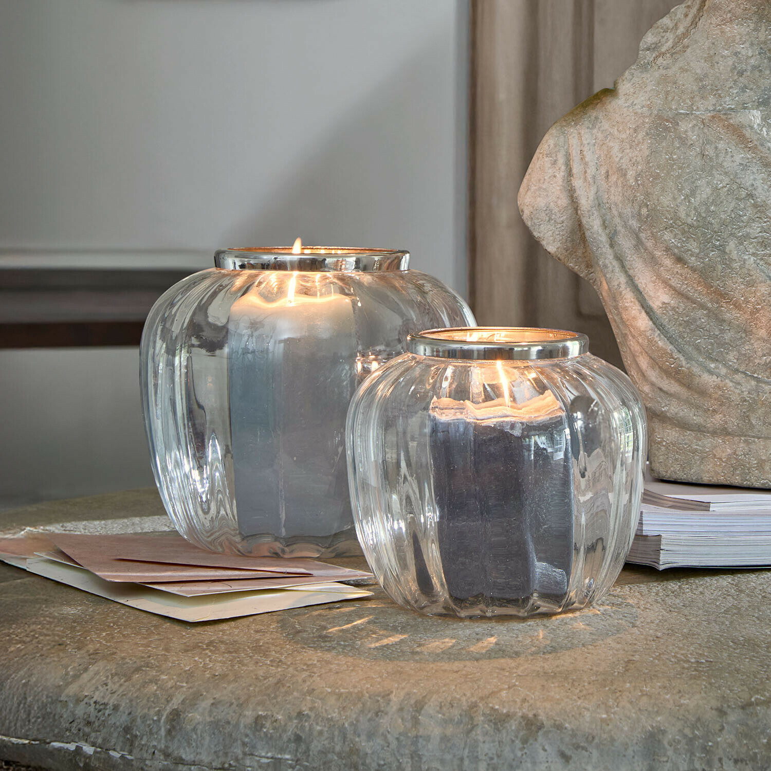 Zwei transparente Glaswindlichter mit brennenden schwarzen Kerzen auf einem Steintisch