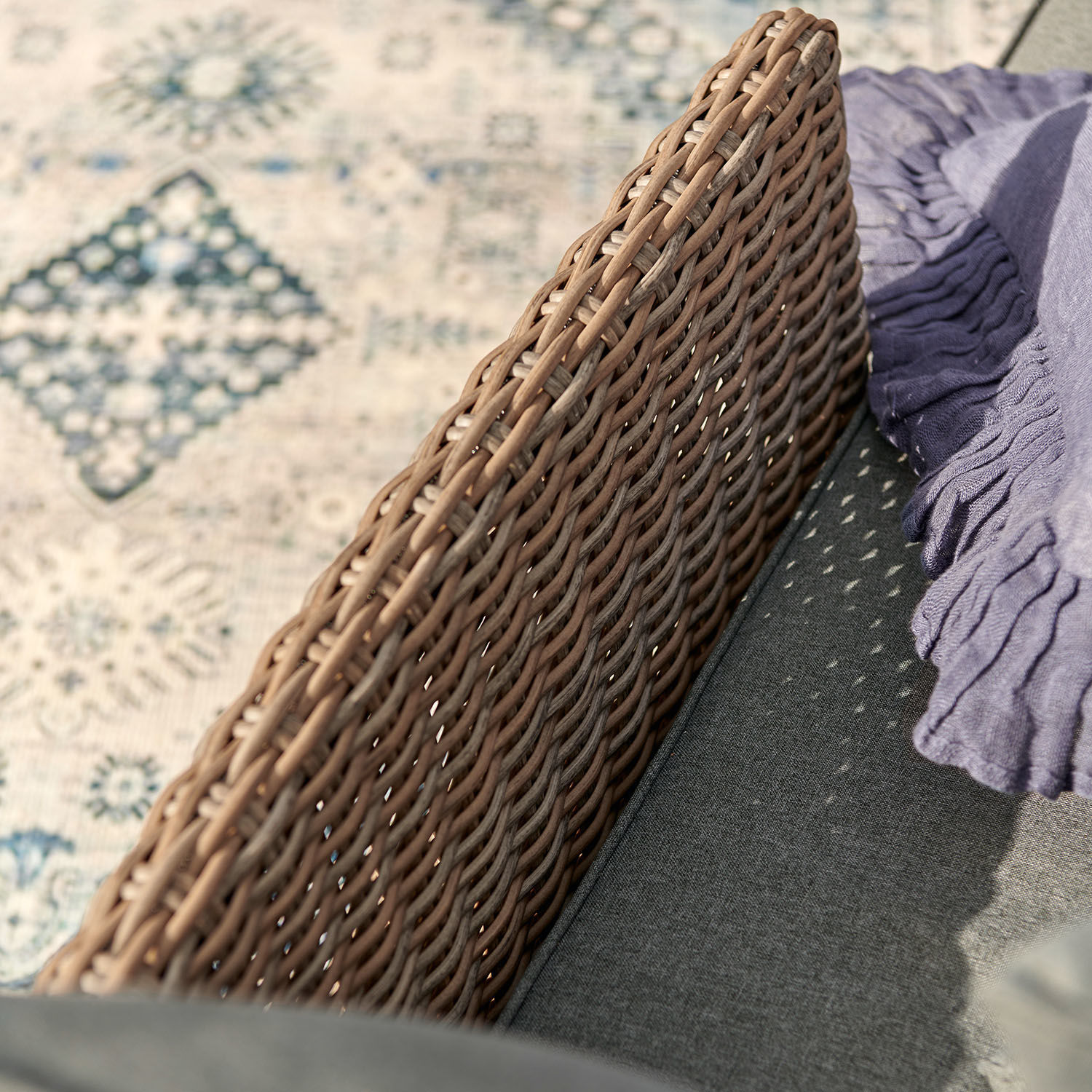 Braunes geflochtenes Rattan-Rückenlehne auf grauem Sitz mit violettem Stoff und Teppich im Hintergrund