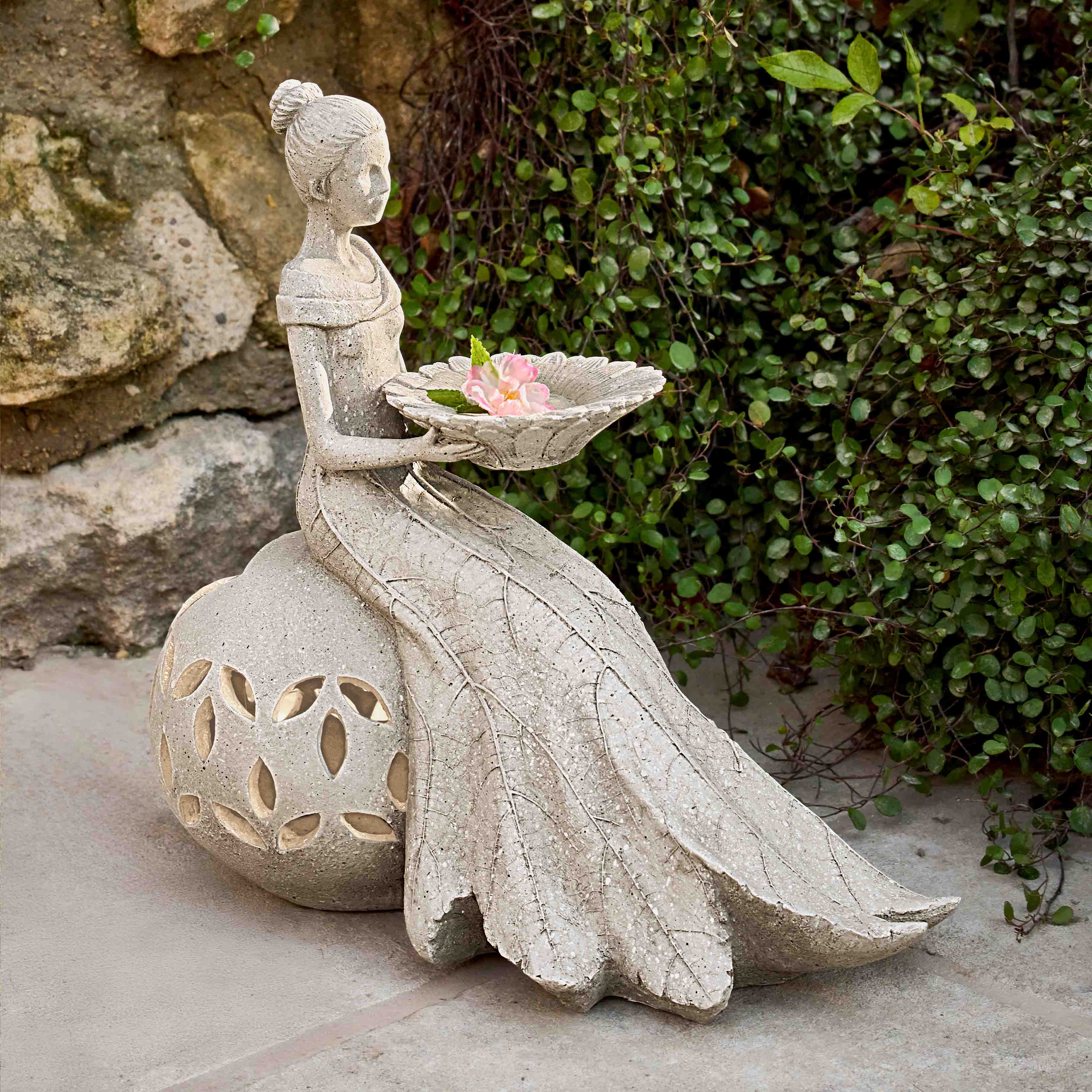 Steinfigur im Garten einer sitzenden Frau mit Schale und Blume als dekorativer Akzent