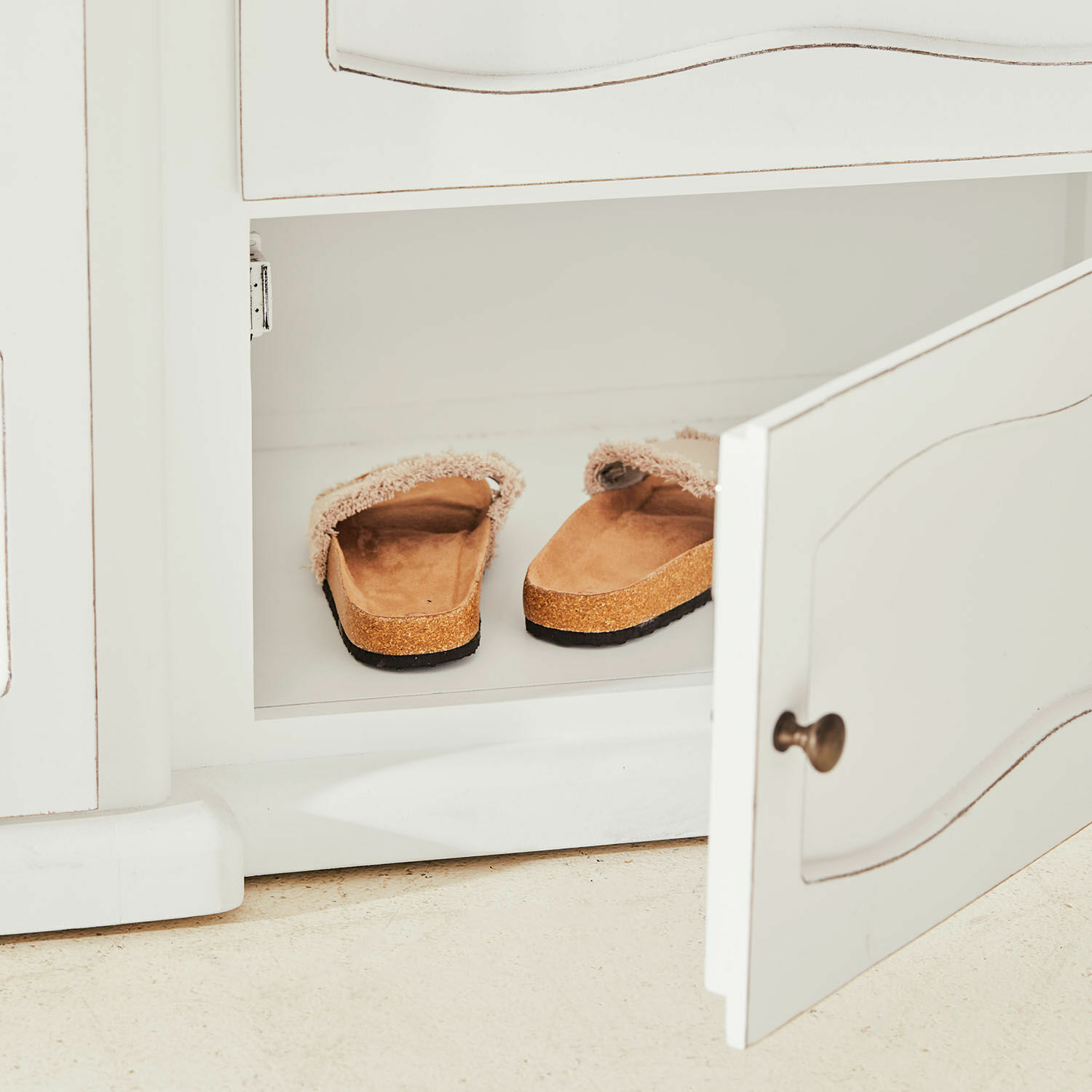 Beige Hausschuhe mit weichem Fell und Korksohle in weißem Schrank auf Boden