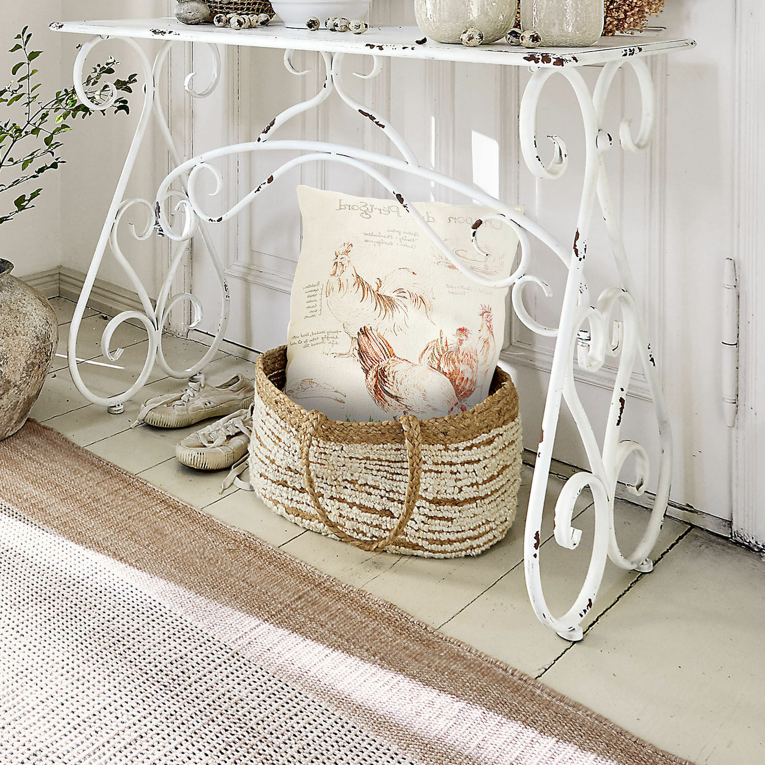 Weißer Metalltisch mit antikem Look und geflochtener Korb mit Kissen im Hühnerdesign, Wohnaccessoire