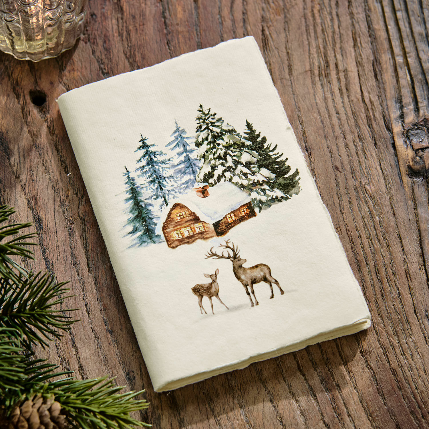 Notizbuch Lorandis Weißes Baumwoll-Geschirrtuch mit Winterhaus- und Hirschmotiv auf Holztisch, festliche Dekoration