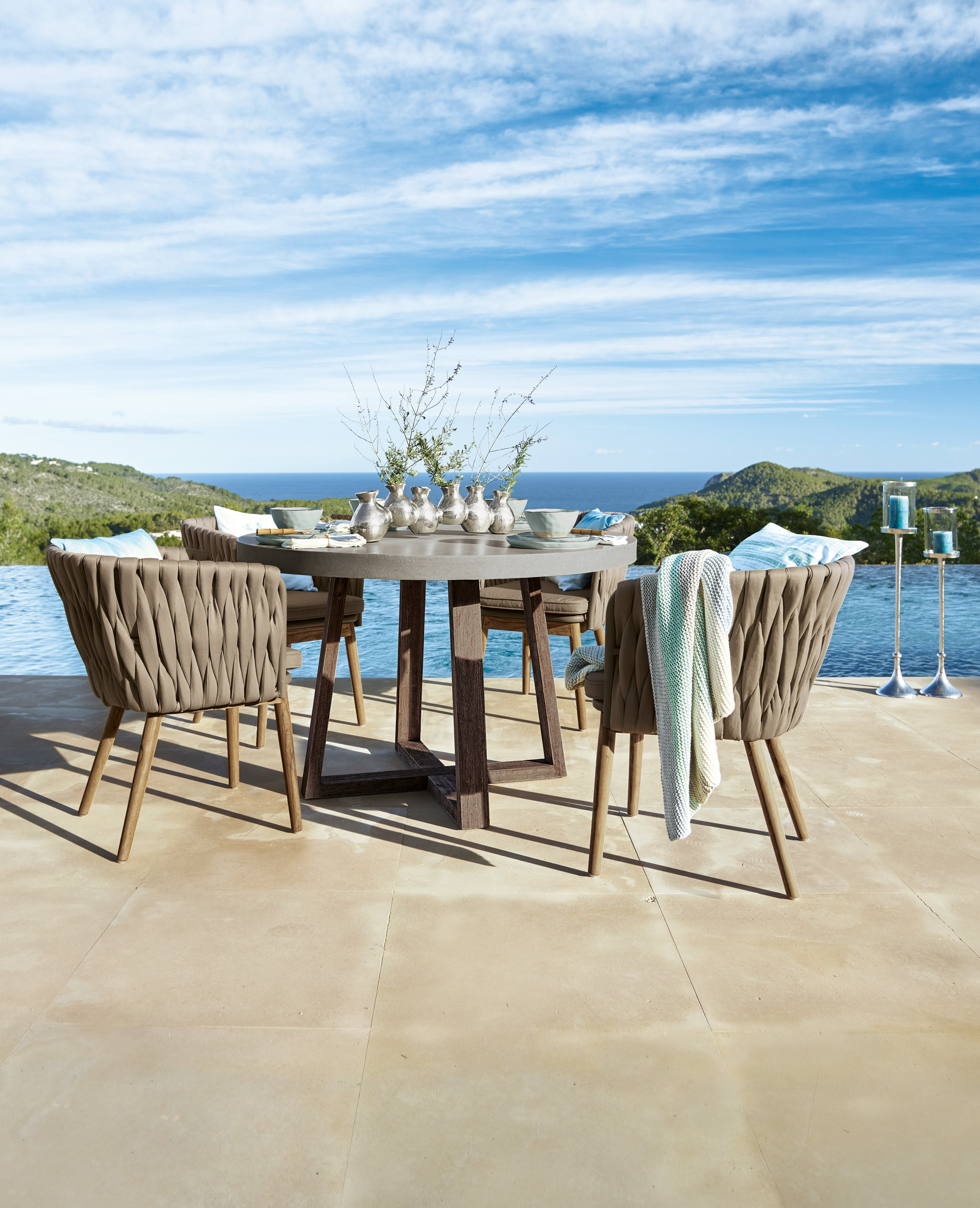 Gartenmöbel-Set mit rundem Tisch und braunen geflochtenen Stühlen auf Terrasse mit Meerblick
