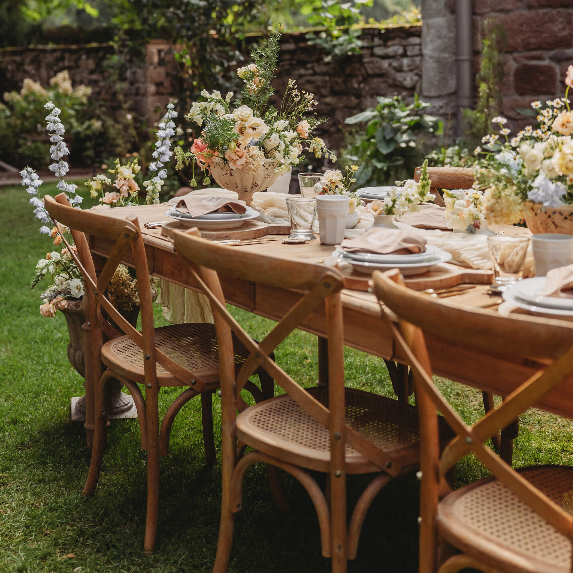 Holz-Gartentisch mit geflochtenen Stühlen und Blumenarrangements auf grünem Rasen