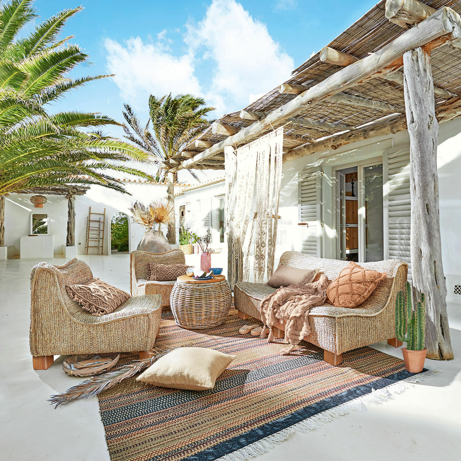Rattansitzgruppe in Naturtönen auf Terrasse mit Kissen und Teppich im Boho-Stil