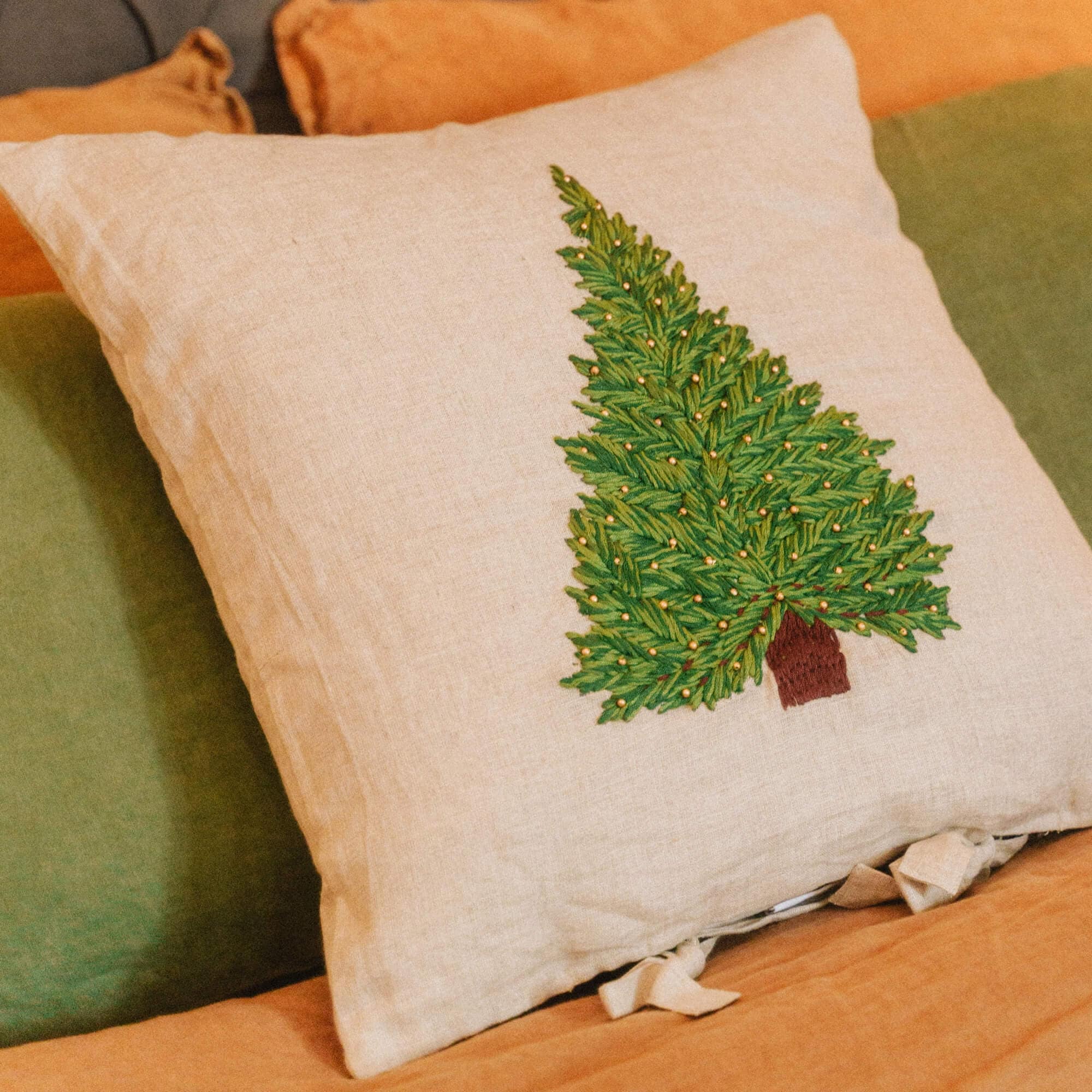 Beige Leinenkissen mit grünem besticktem Tannenbaum auf orange-grüner Bettwäsche