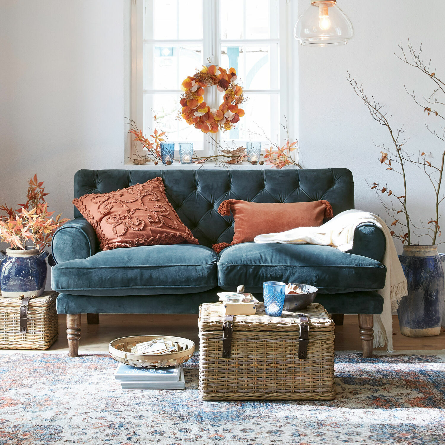 Sofa Carme Samtsofa in Dunkelblau mit rostfarbenen Kissen und Korbtisch in gemütlichem Wohnzimmer