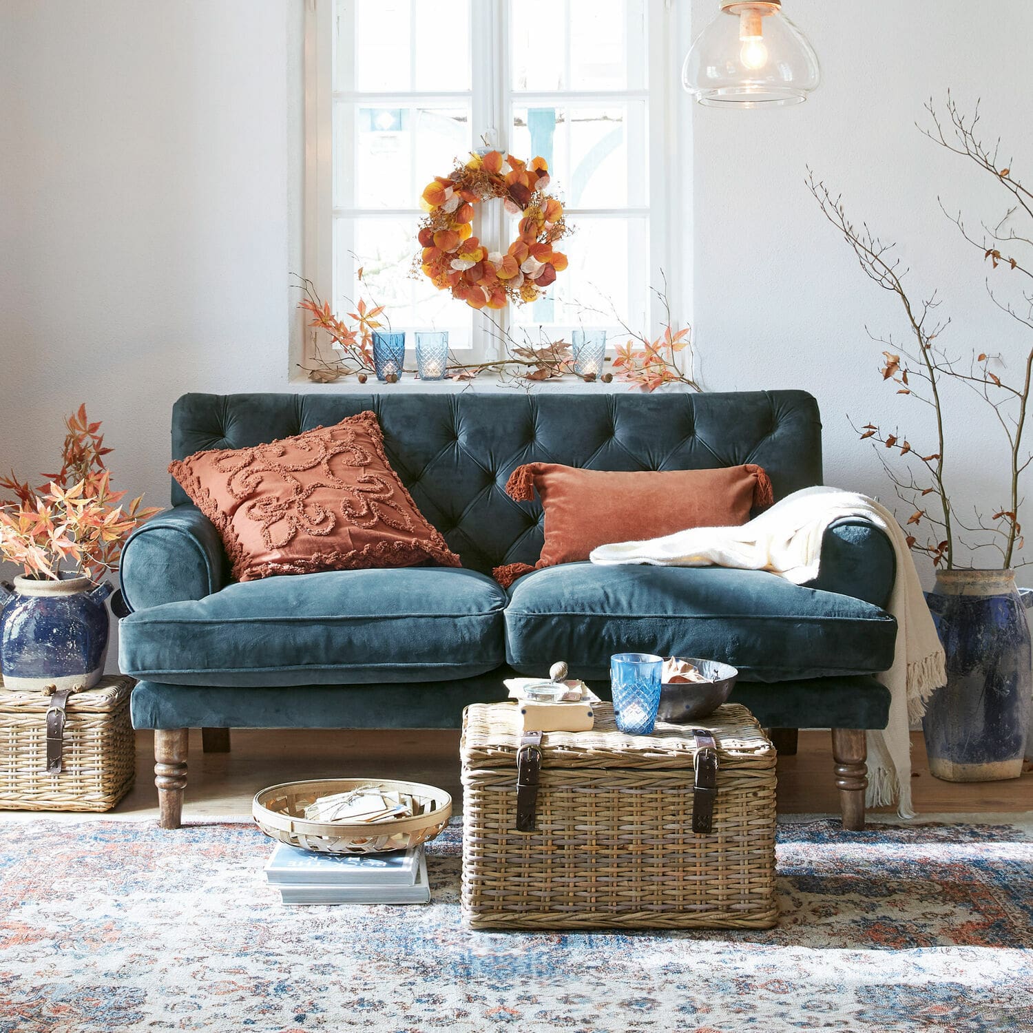 Sofa Carme Samtsofa in Dunkelblau mit rostfarbenen Kissen und Korbtisch in gemütlichem Wohnzimmer