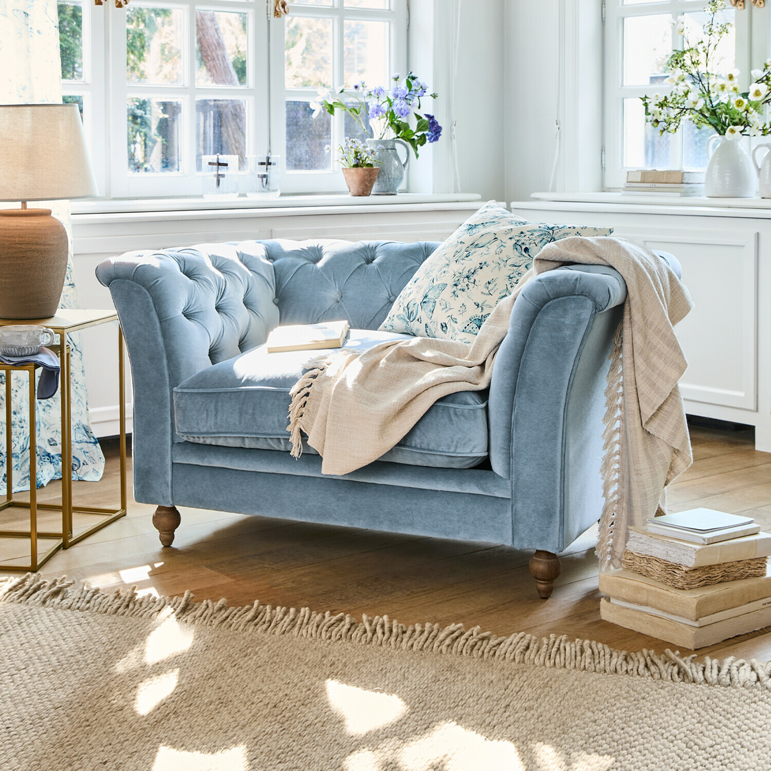 Sofa Clères Zweisitziges Sofa aus blauem Samt mit gesteppter Rückenlehne und beiger Decke in hellem Wohnzimmer