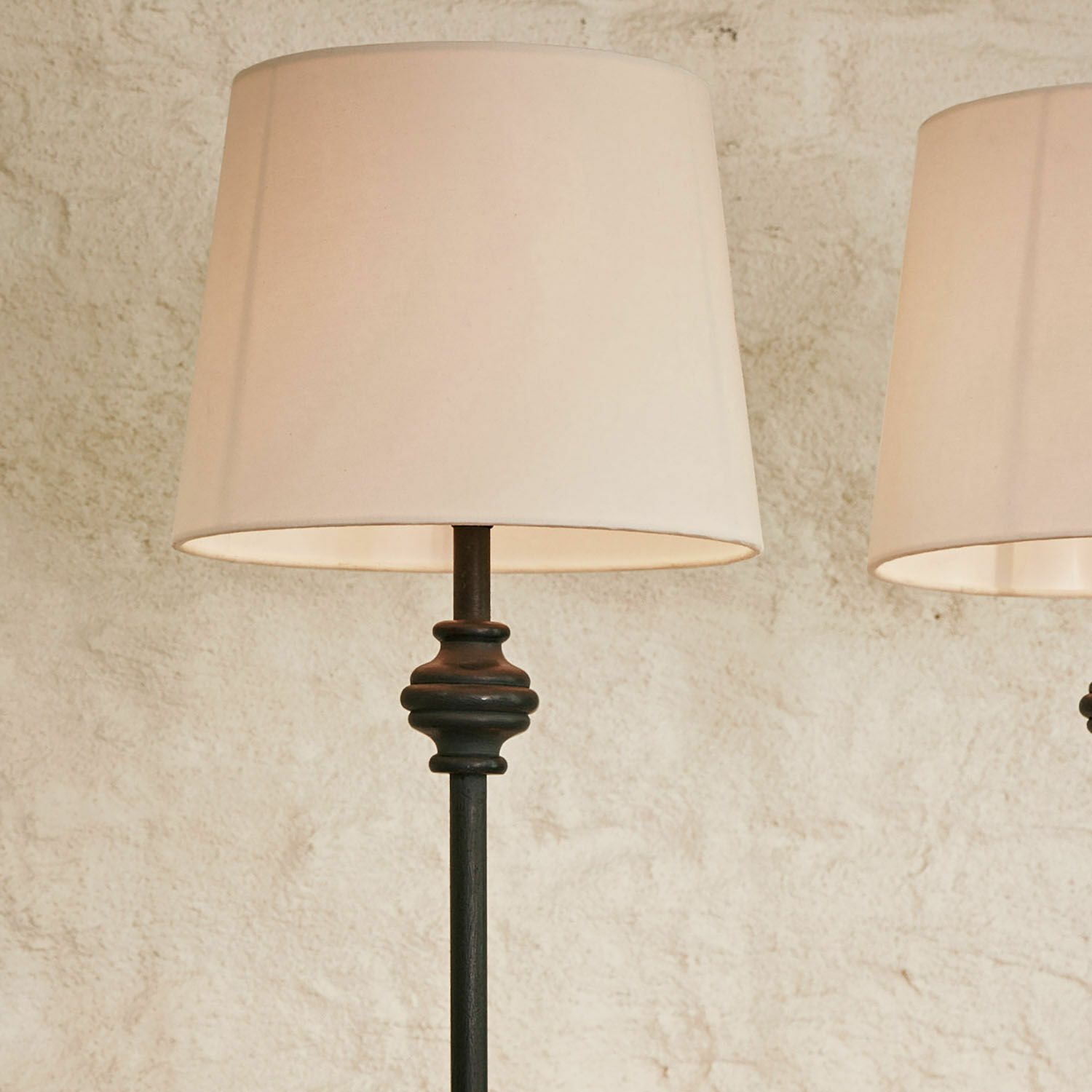 Stehlampe aus schwarzem Metall mit cremefarbenem Lampenschirm vor hellem Wandhintergrund