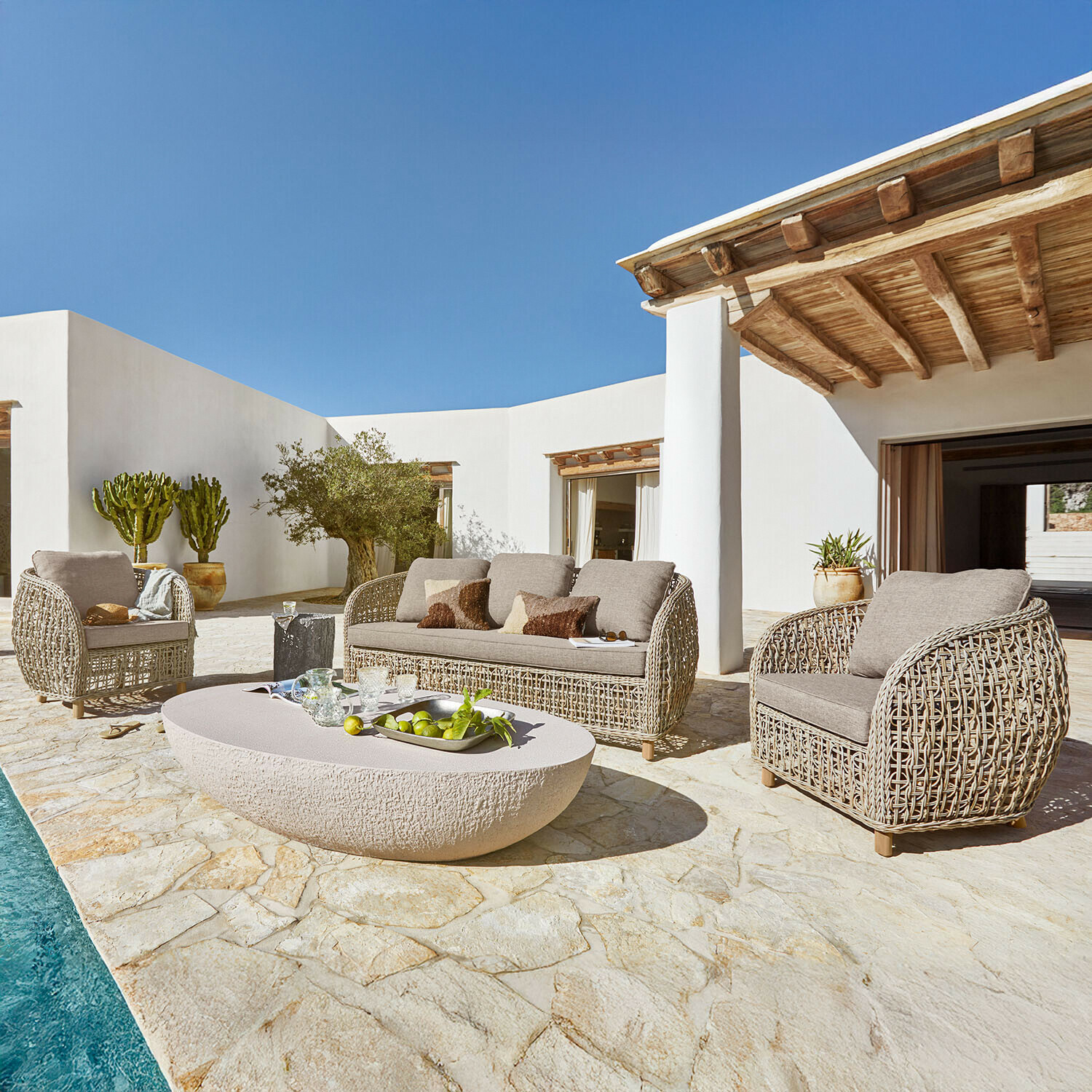 Sitzgruppe Ventiglio Beiges Rattan-Gartenmöbel-Set mit Polstern auf Stein-Terrasse neben Pool bei Sonnenschein