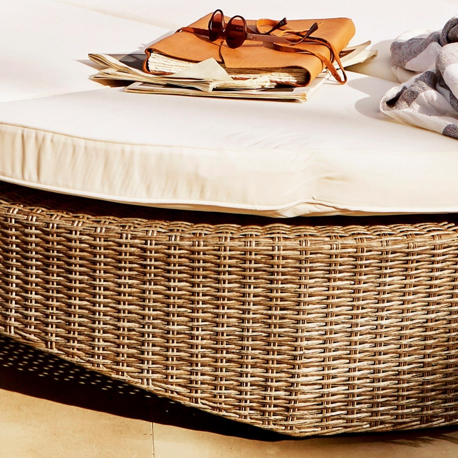 Beige Polster auf Rattan-Sitzfläche mit Sonnenbrille und Notizbuch darauf