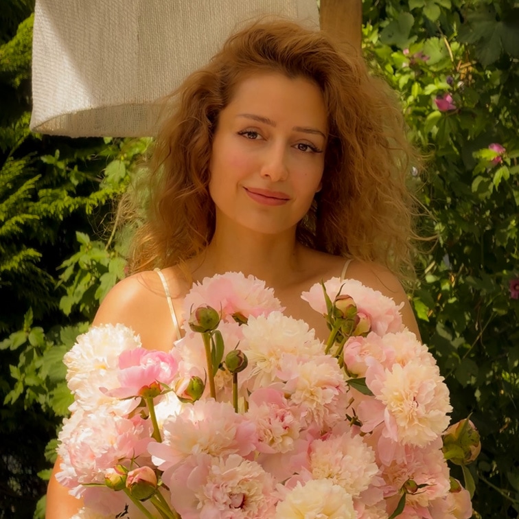 Frau mit langen Haaren hält großen Strauß rosa Pfingstrosen vor grünem Gartenhintergrund