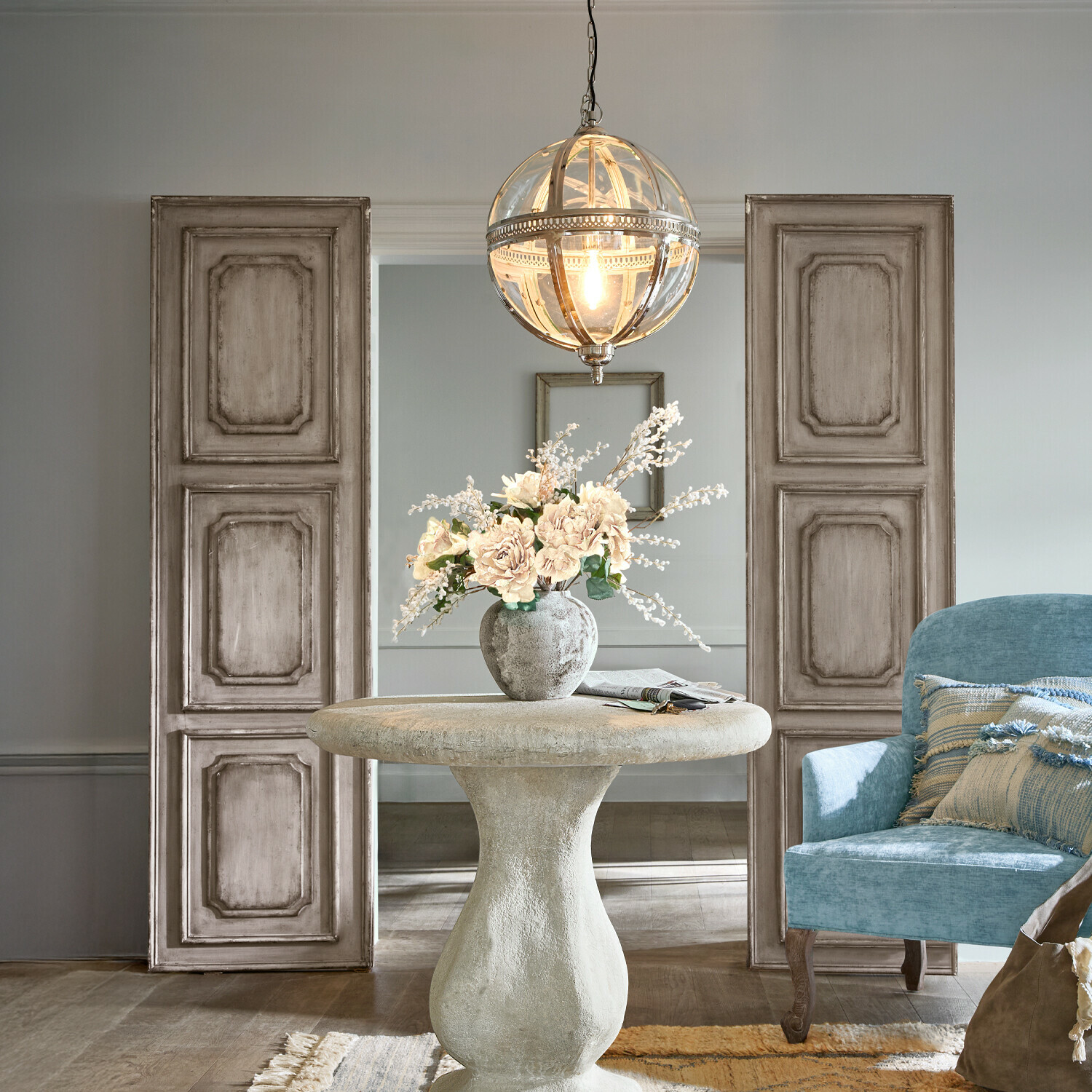 Runder Betontisch mit Blumenvase, hängende Glaskugel und blauem Sessel im Wohnzimmer